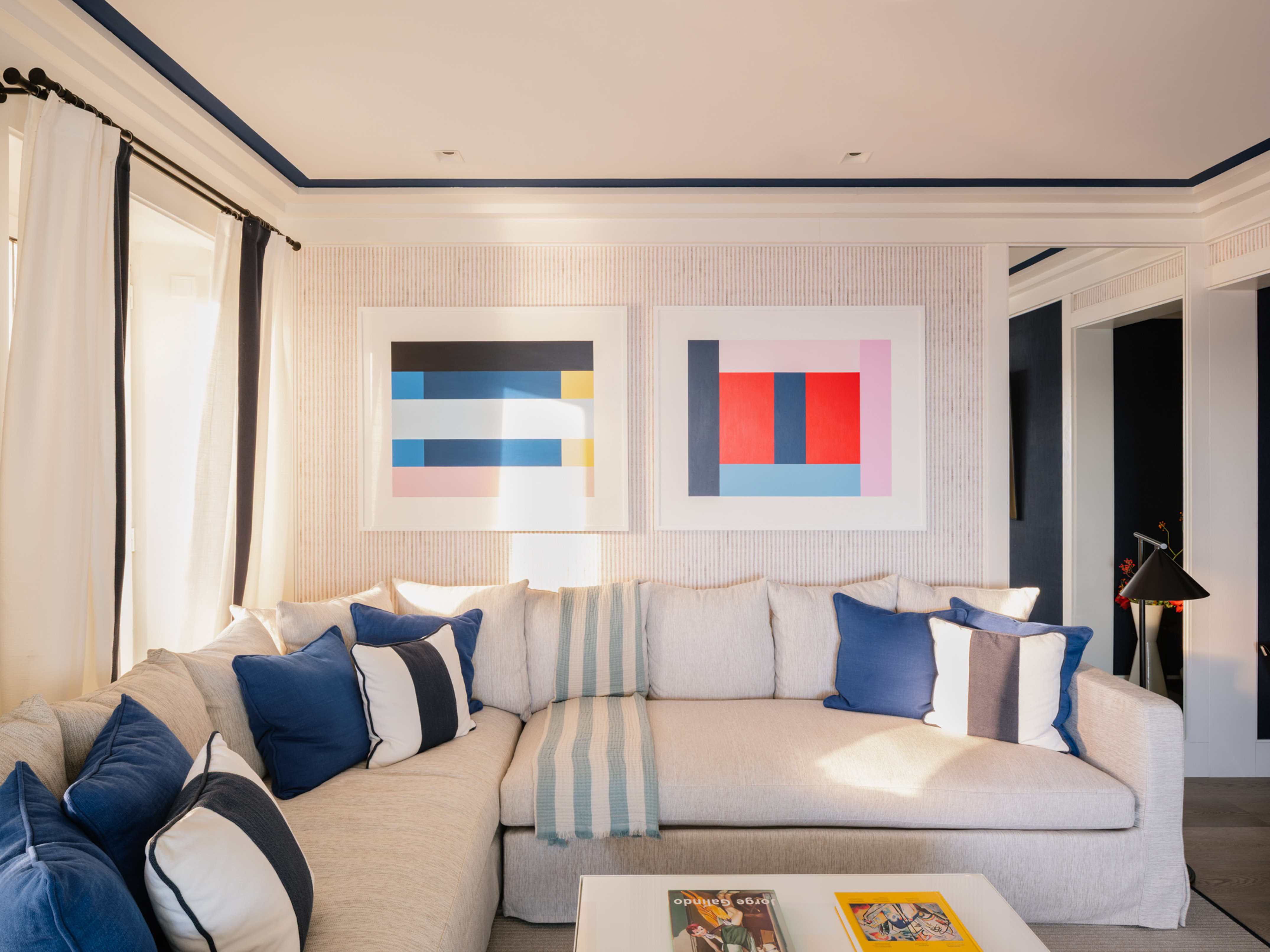 Modern living room with beige sectional sofa, blue pillows, and geometric art.