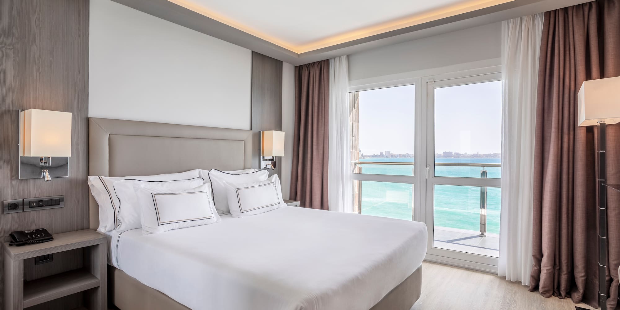 a bed with white sheets and a window with a view of the ocean