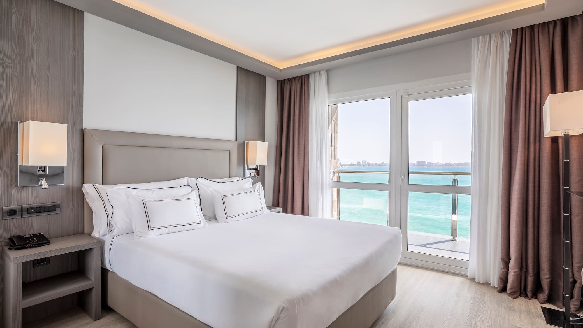 a bed with white sheets and a window with a view of the ocean