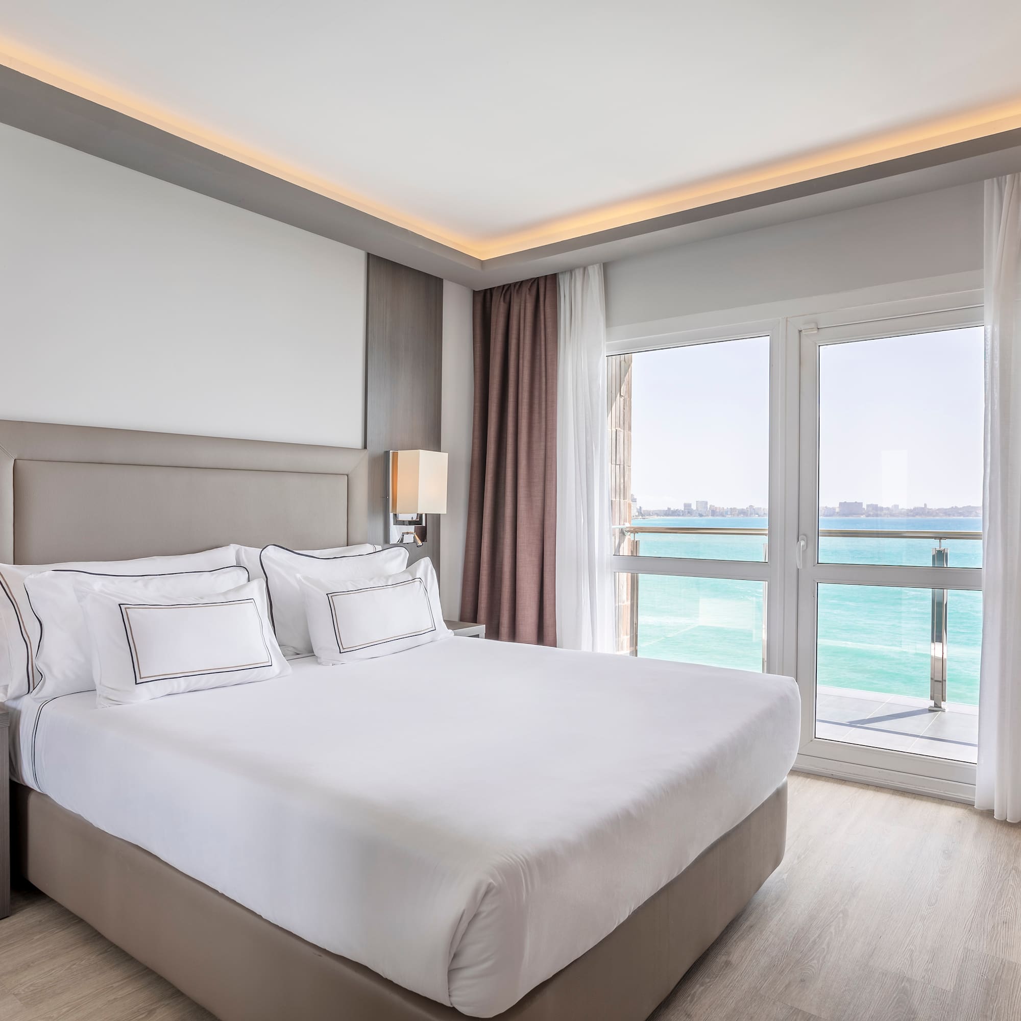 a bed with white sheets and a window with a view of the ocean