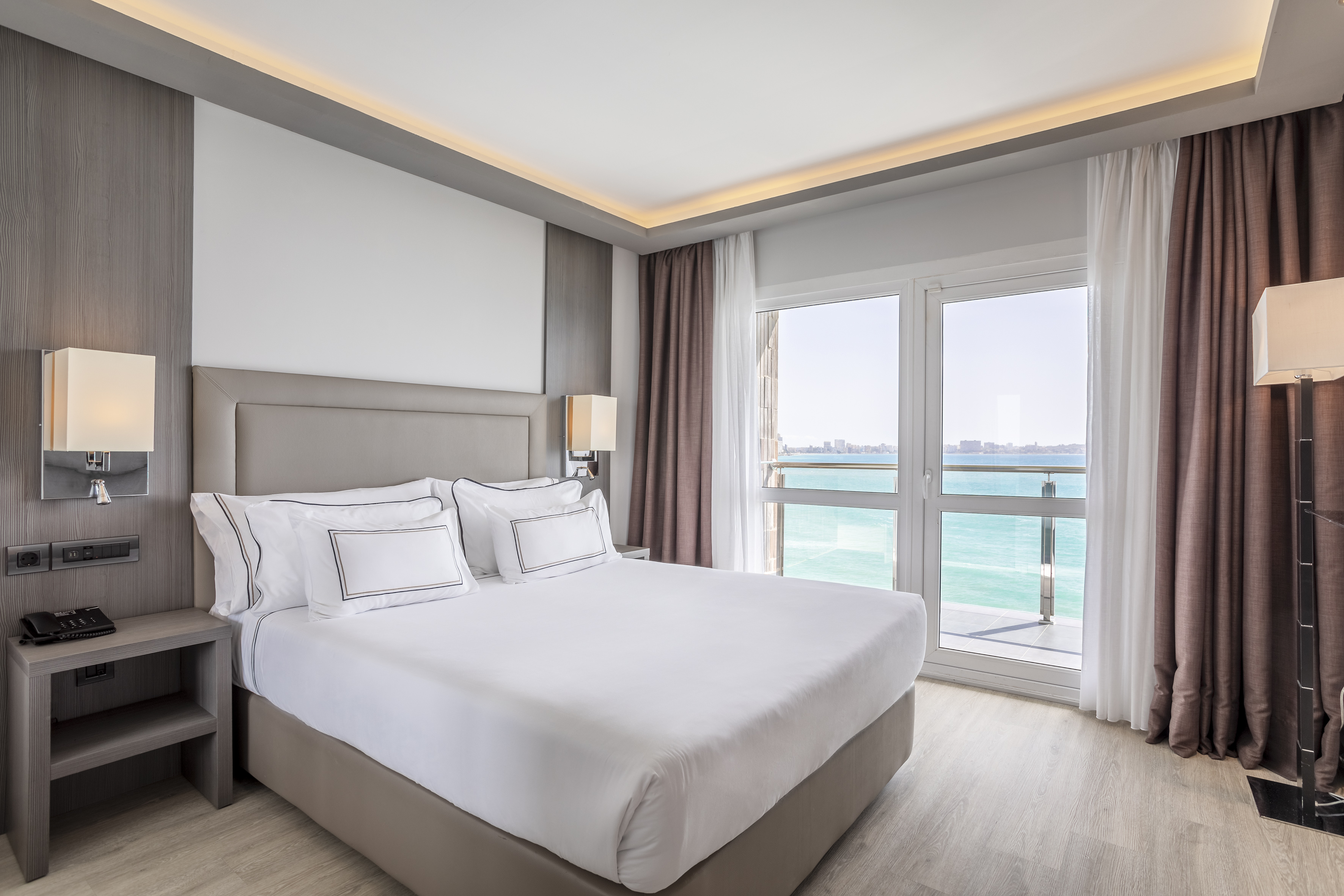 Contemporary hotel bedroom with sea view balcony and comfortable bed.