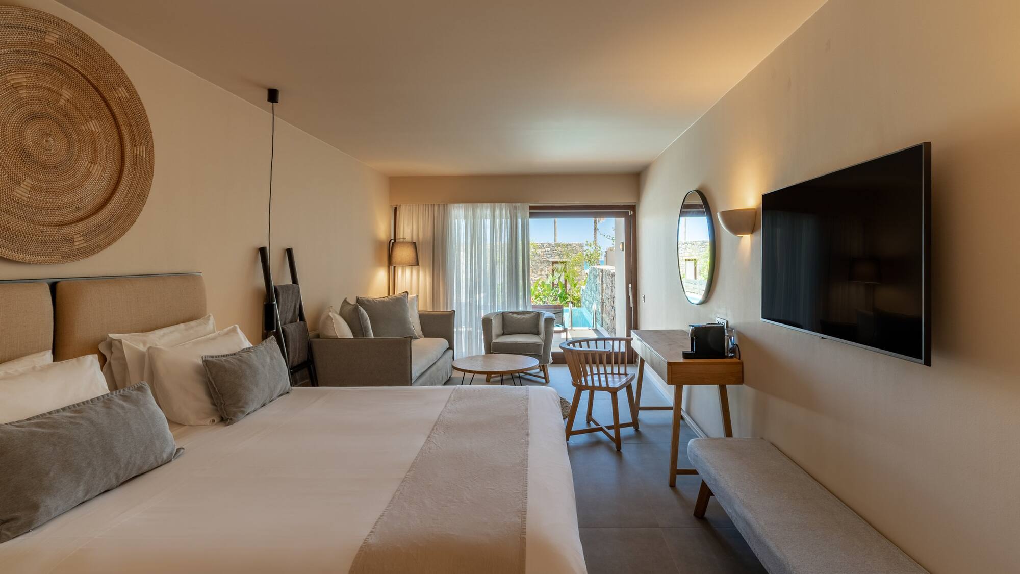 Contemporary hotel suite with bed, sitting area, TV, and private outdoor pool.