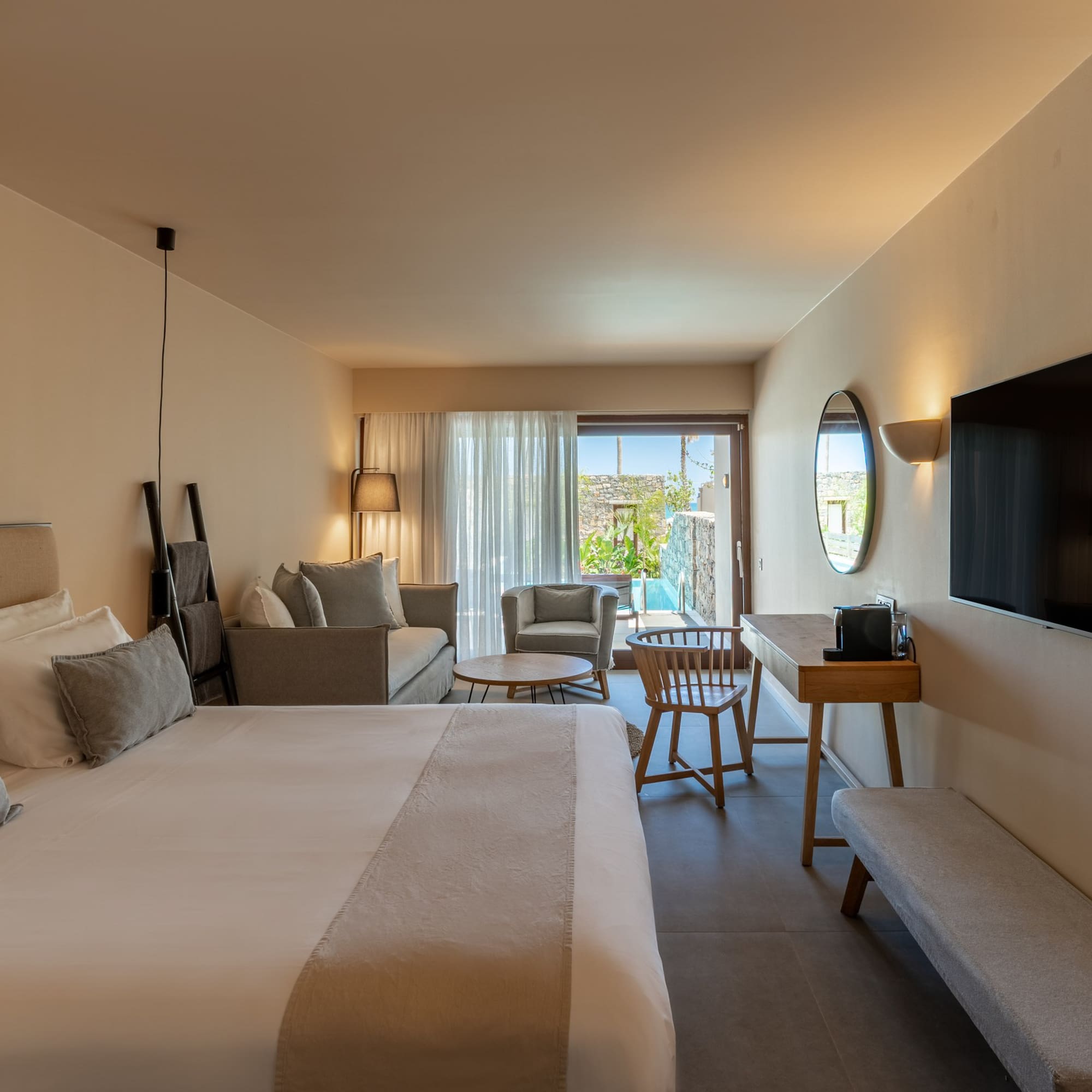 Contemporary hotel suite with bed, sitting area, TV, and private outdoor pool.