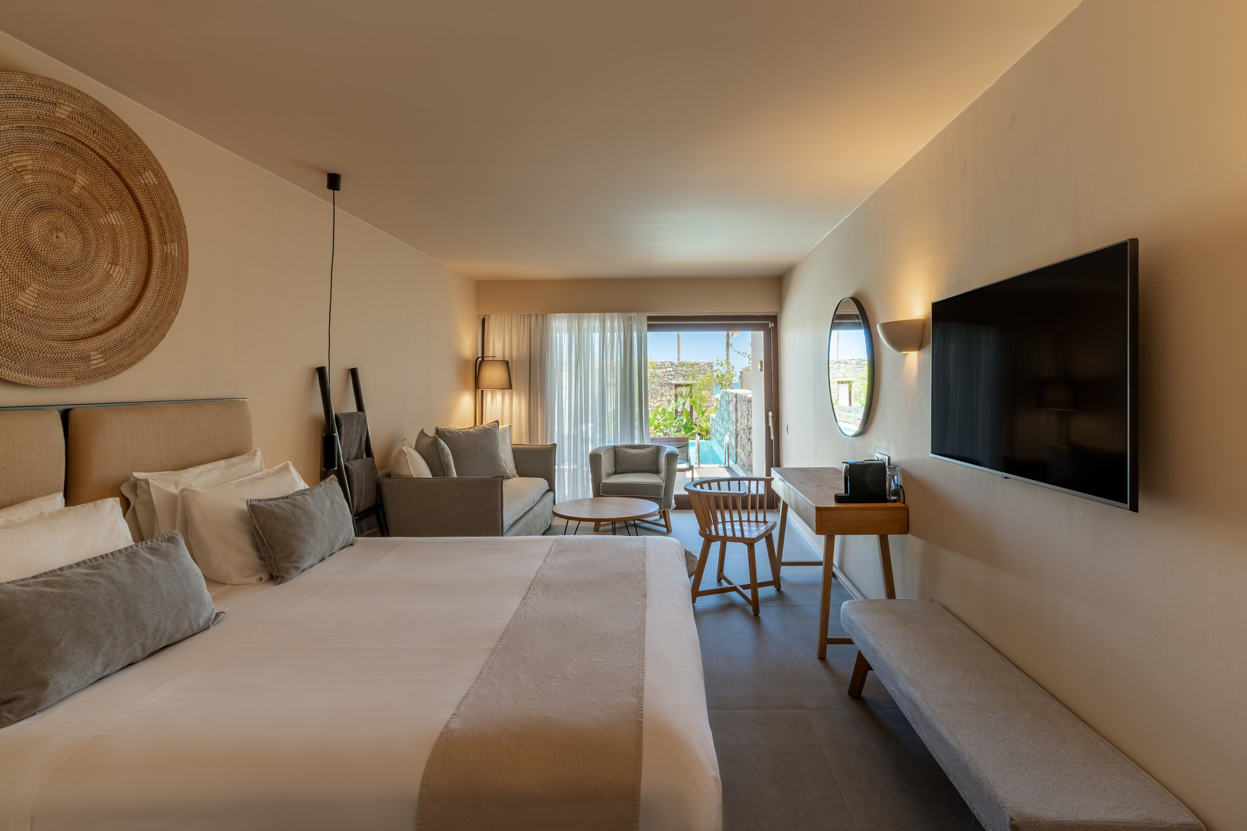 Contemporary hotel suite with bed, sitting area, TV, and private outdoor pool.
