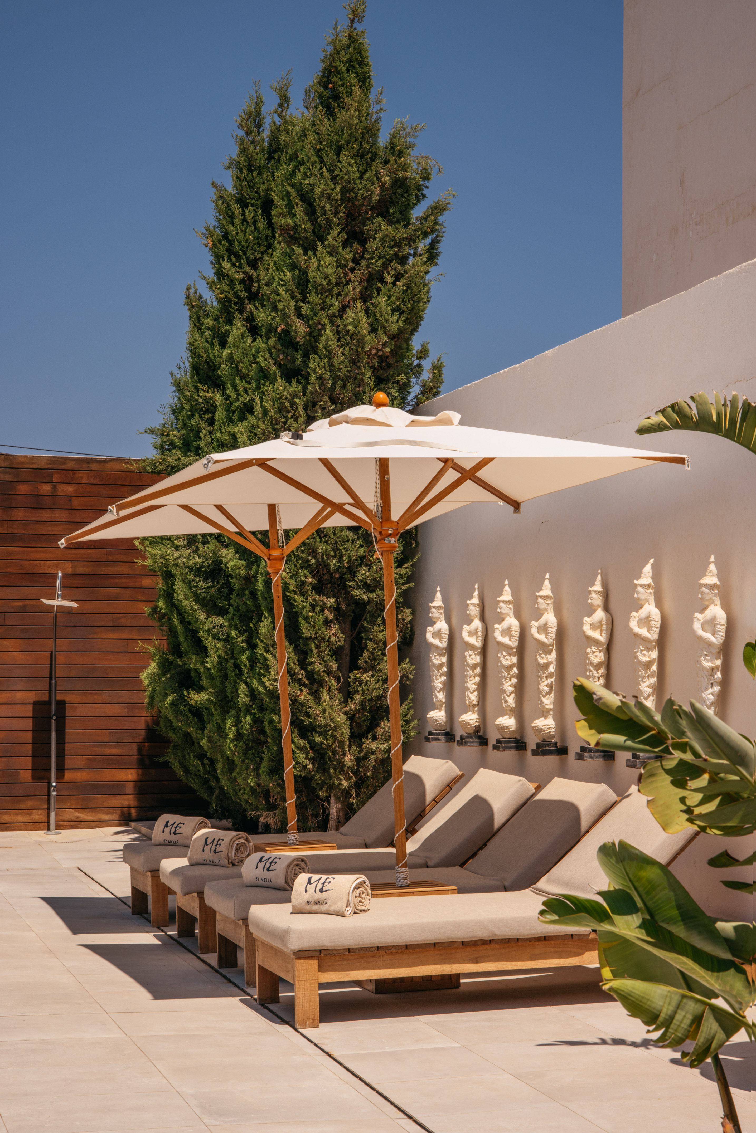 ME by Melia luxury resort patio with sunbeds, umbrellas, and wall statues.