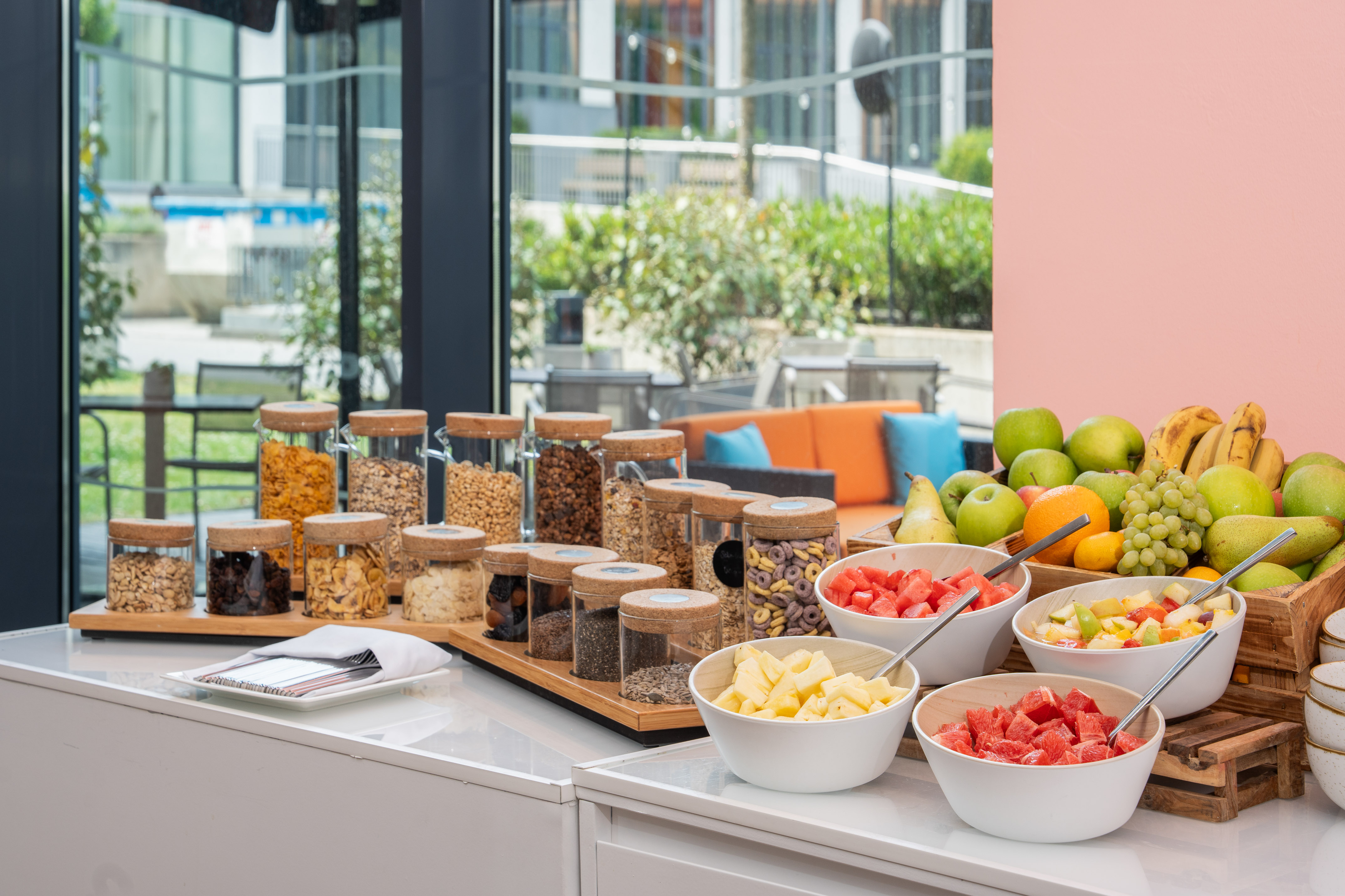 Breakfast buffet: fresh fruit, fruit bowls, and jars of cereals, nuts, and seeds.