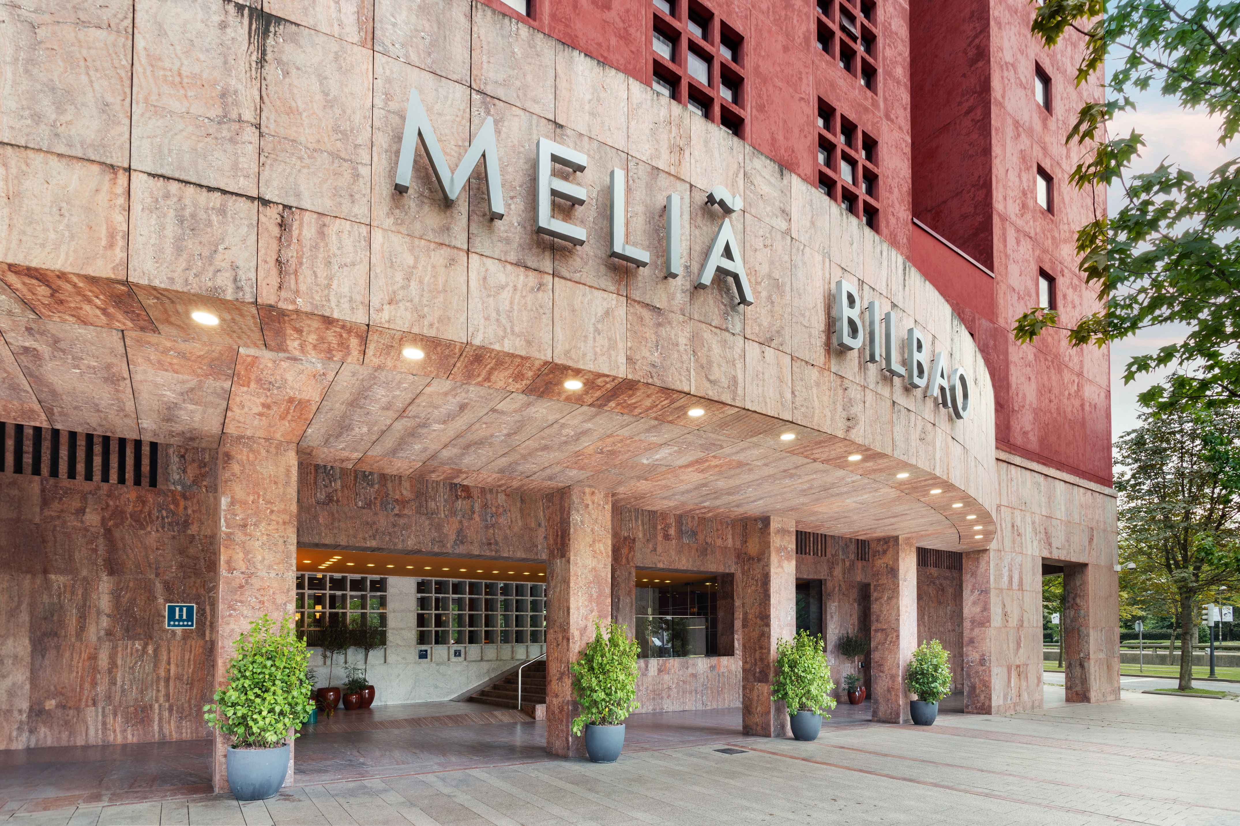 Melia Bilbao hotel facade, stone and red, with covered entrance.
