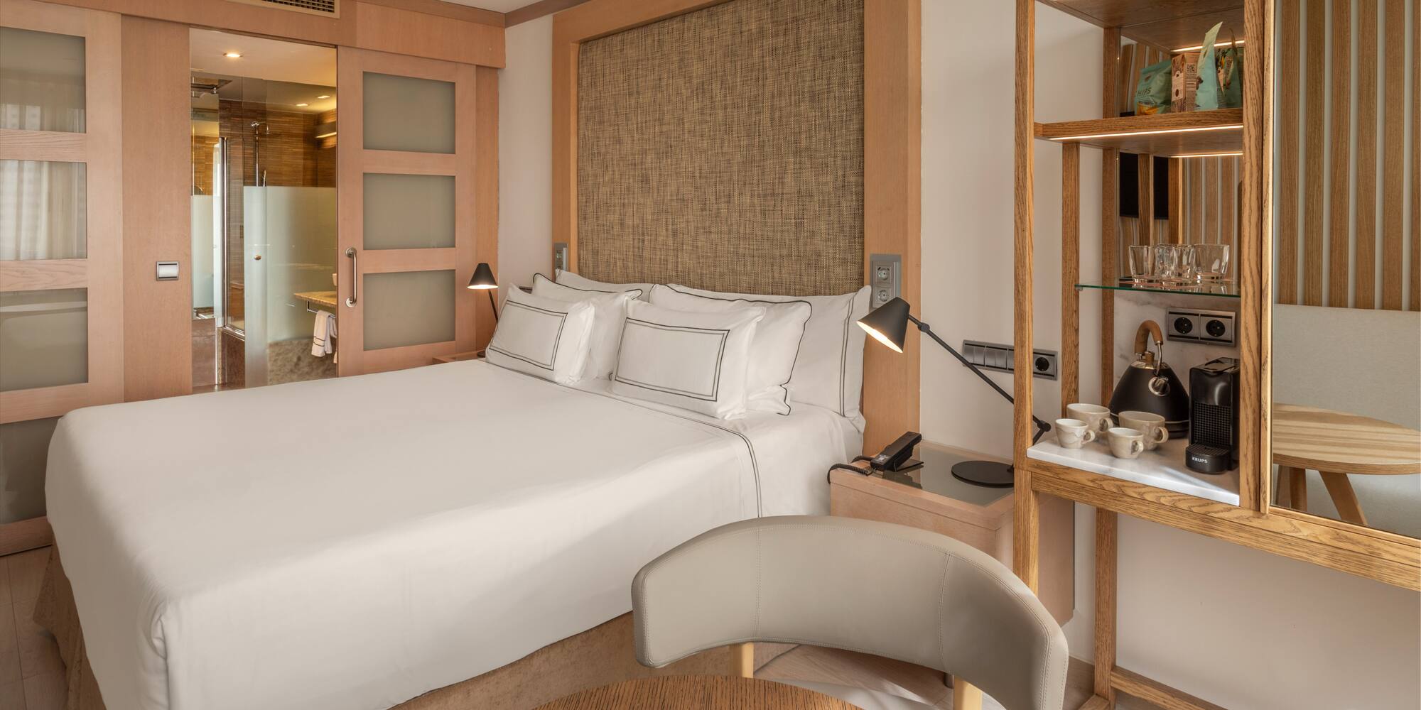 Modern hotel bedroom with large bed, coffee station, and sliding bathroom door.