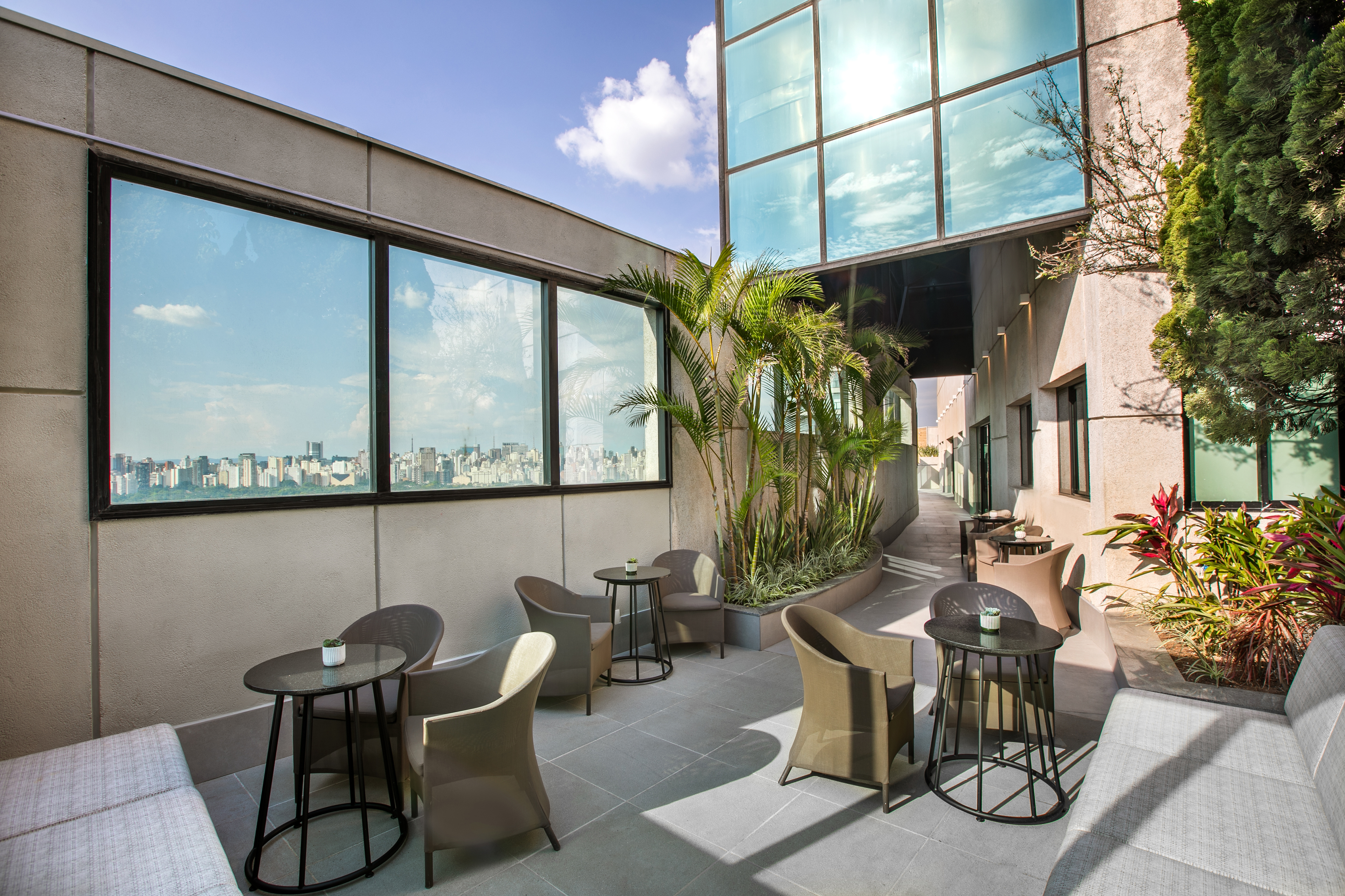 Modern rooftop terrace with city skyline view, outdoor seating, and palm trees.