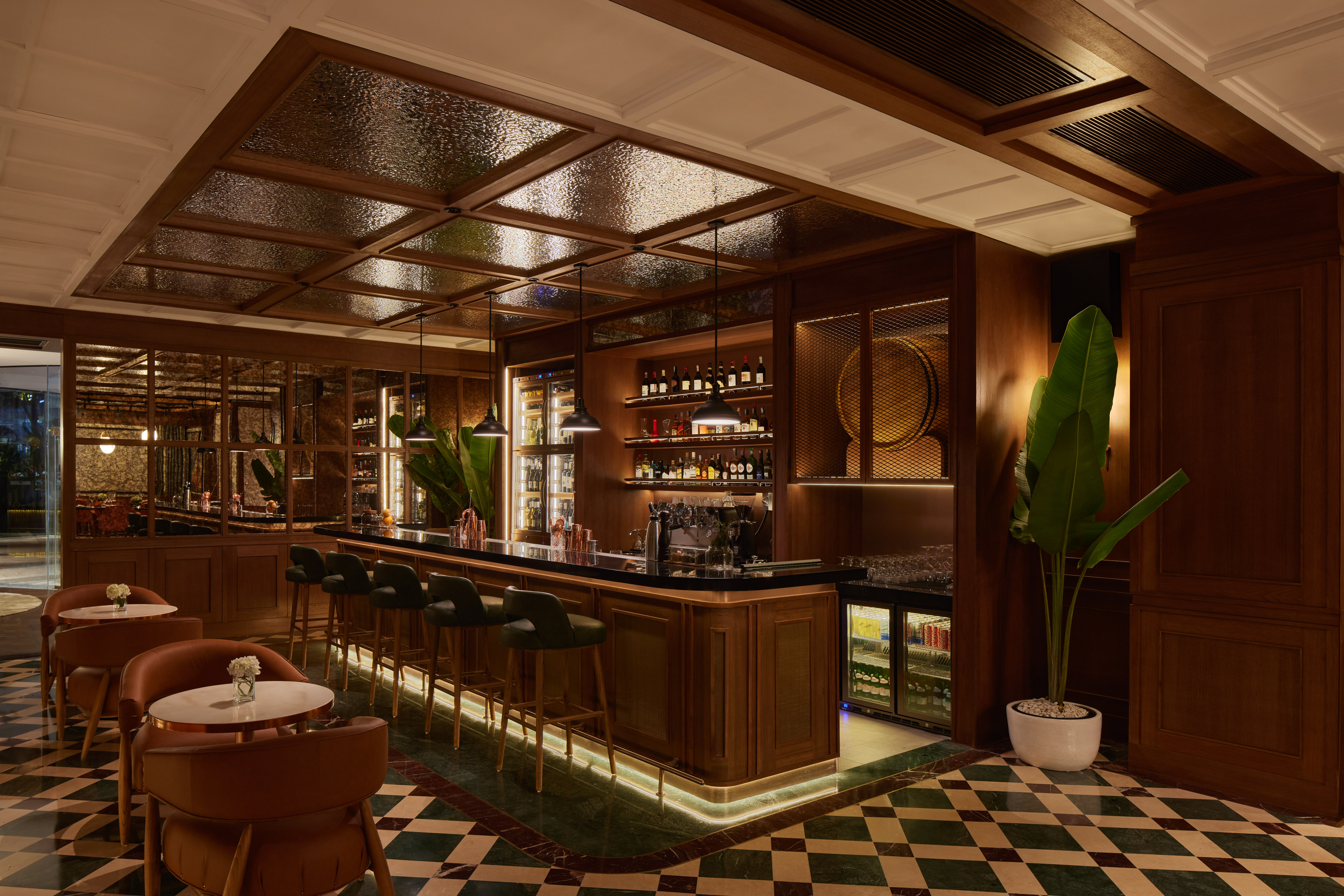 Luxurious cocktail lounge with dark wood, green stools, and marble floor.