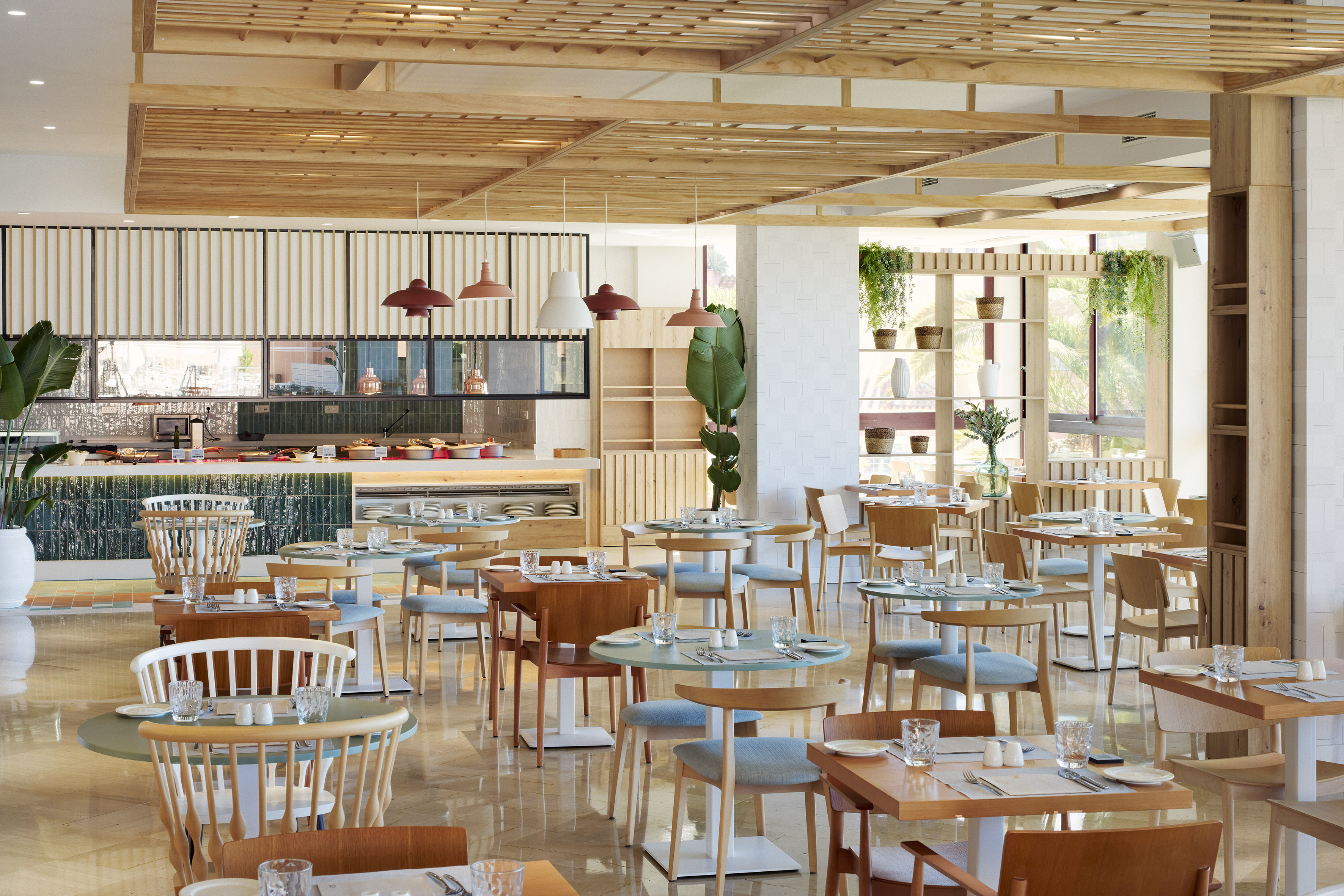 Modern restaurant interior with wooden ceiling, dining tables, and buffet area.
