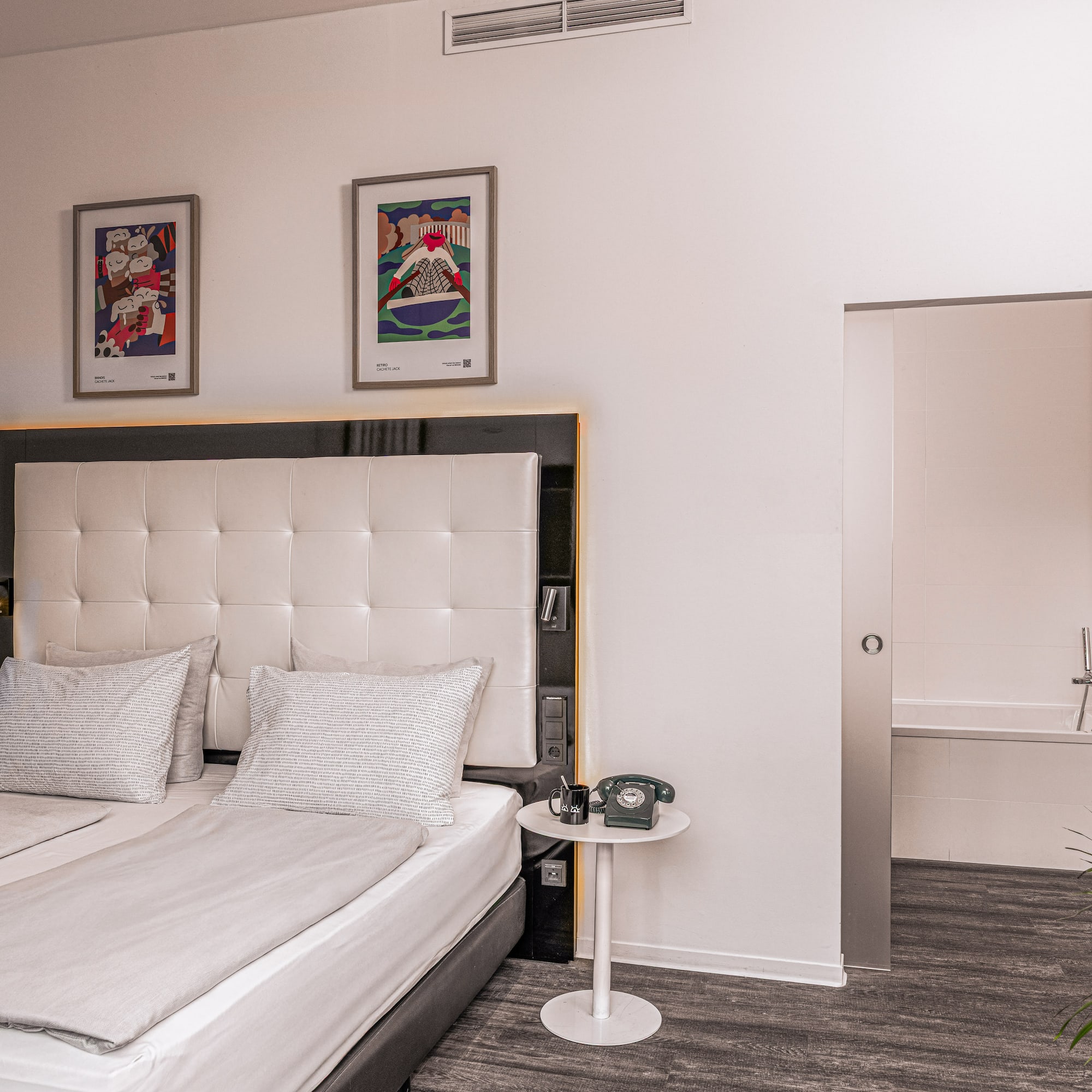 Contemporary hotel room with twin beds, framed art, and an ensuite bathroom.