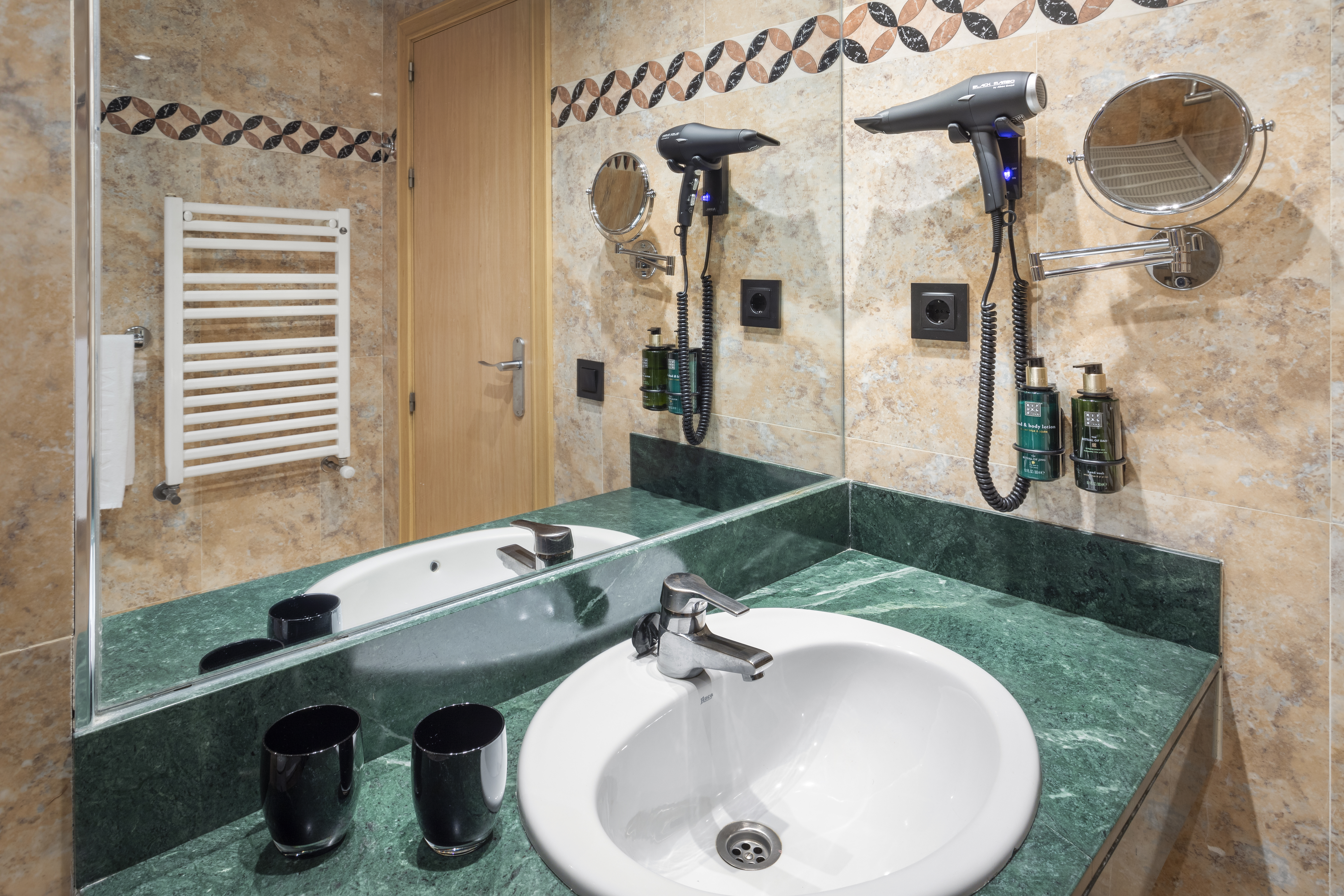 Modern hotel bathroom with green marble vanity, sink, mirror, and hairdryer.
