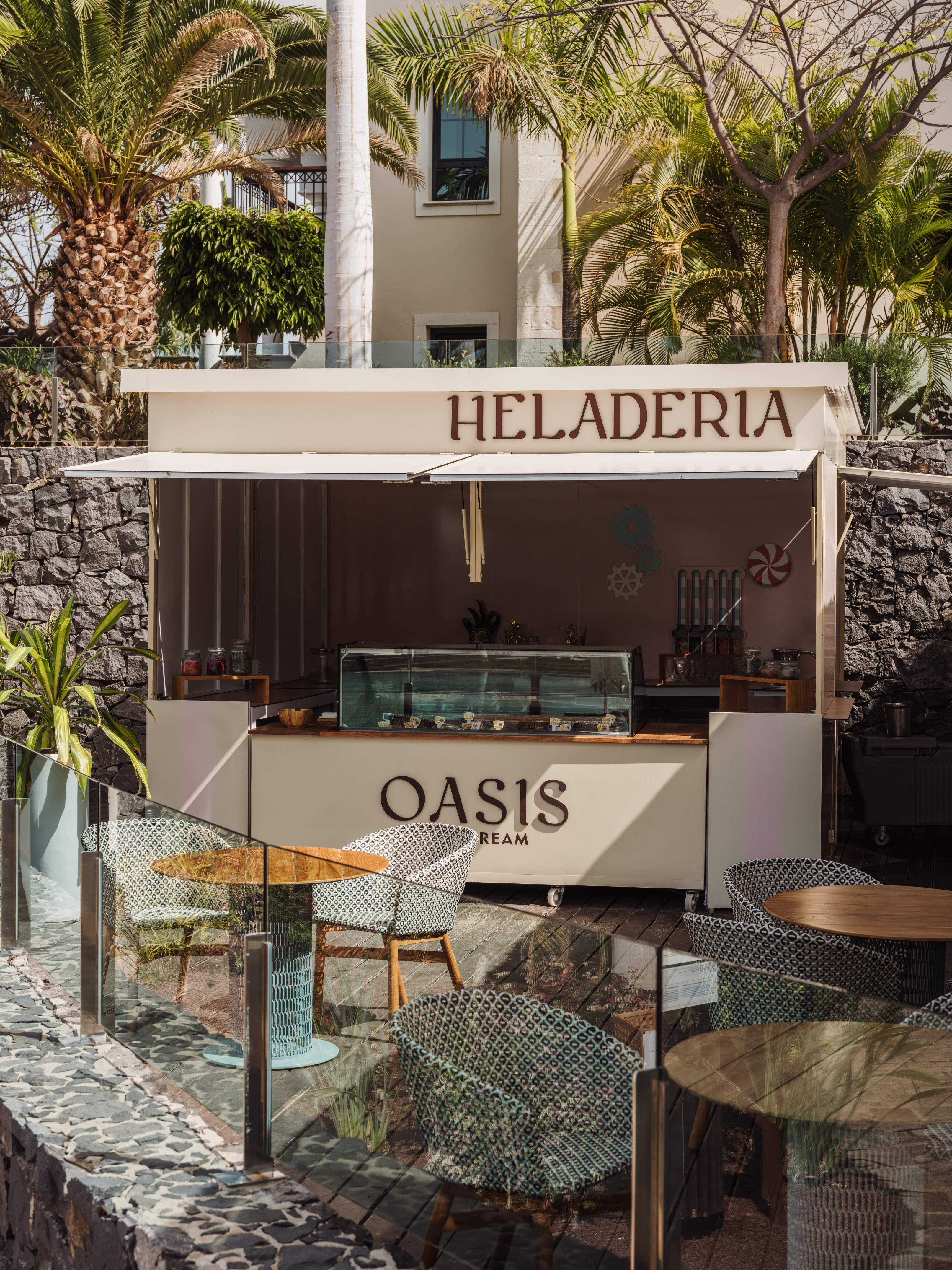 Oasis Heladeria stand with outdoor seating area and palm trees.