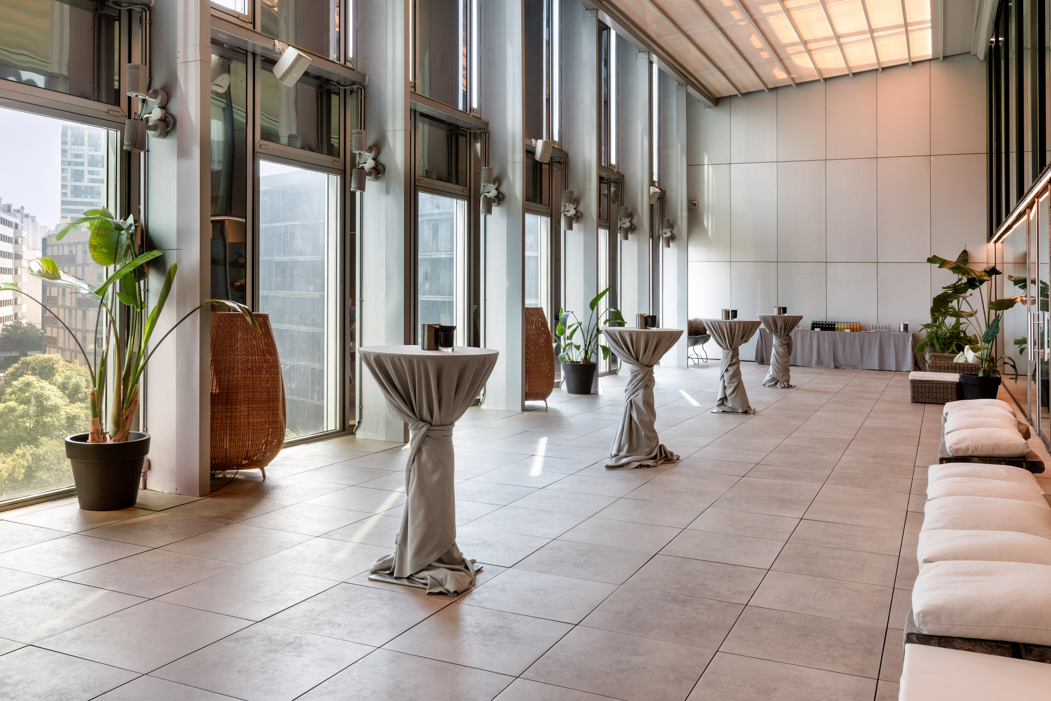 Modern reception hall with cocktail tables, city views, and plants.
