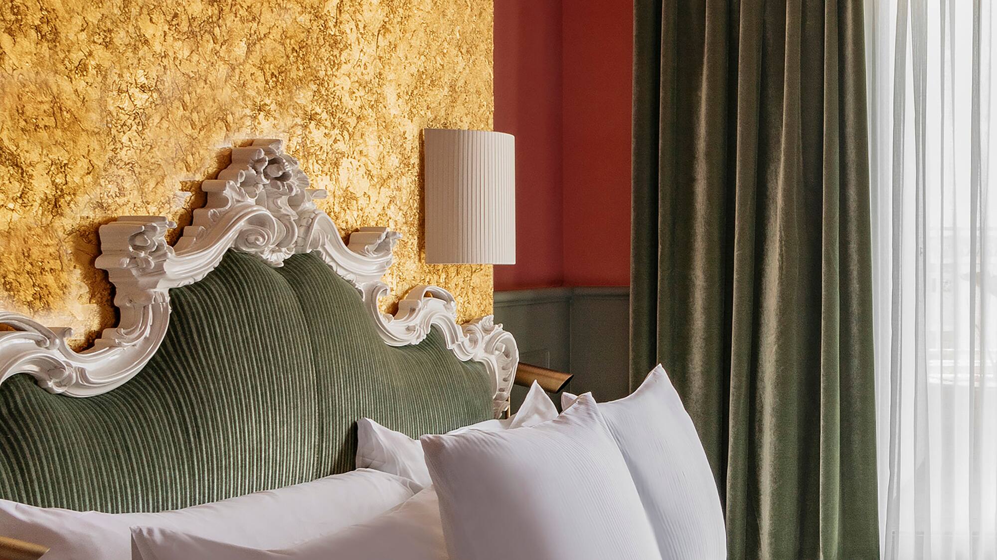 a bed with white pillows and a lamp in a room with a gold wall