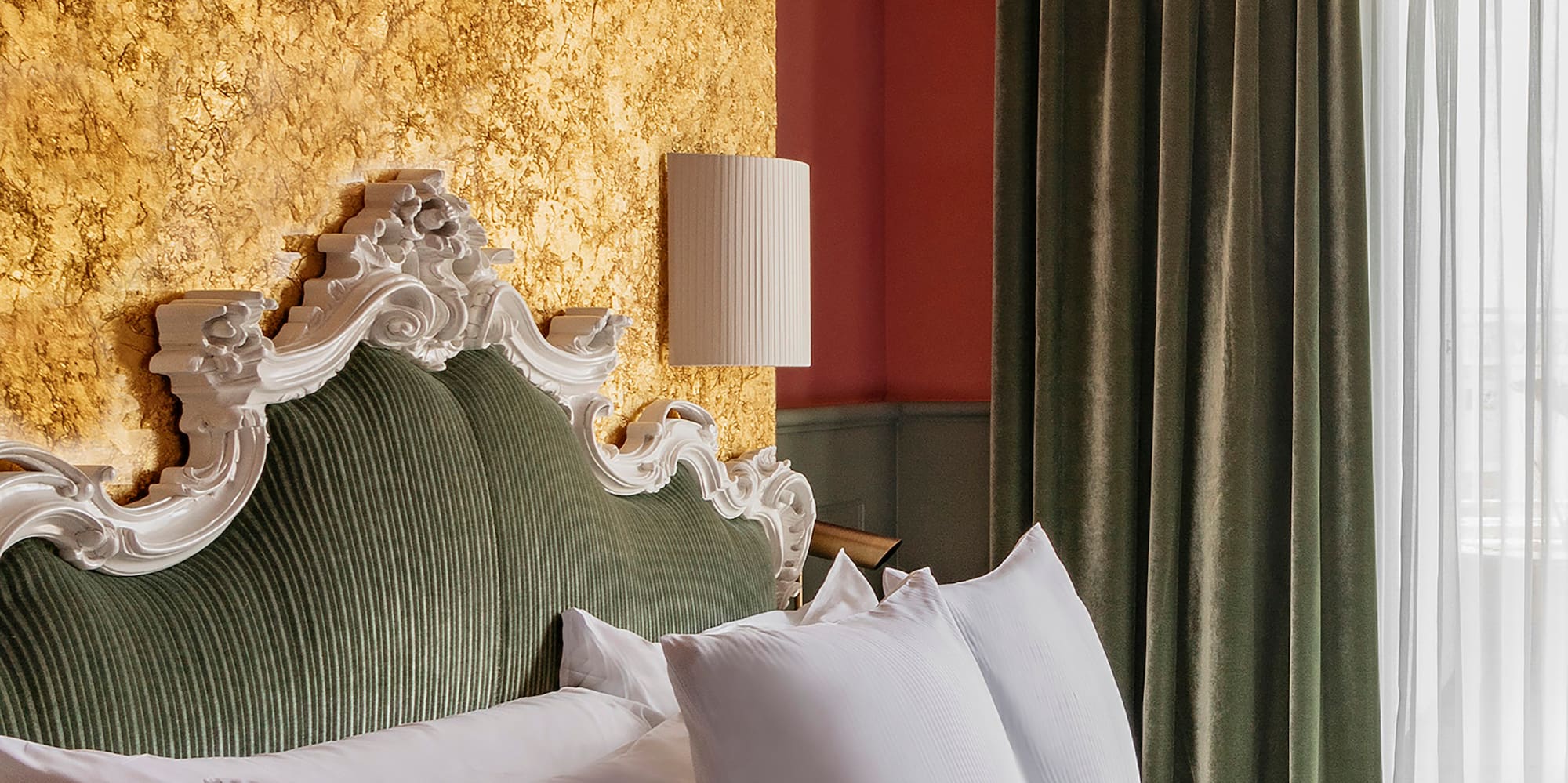 a bed with white pillows and a lamp in a room with a gold wall