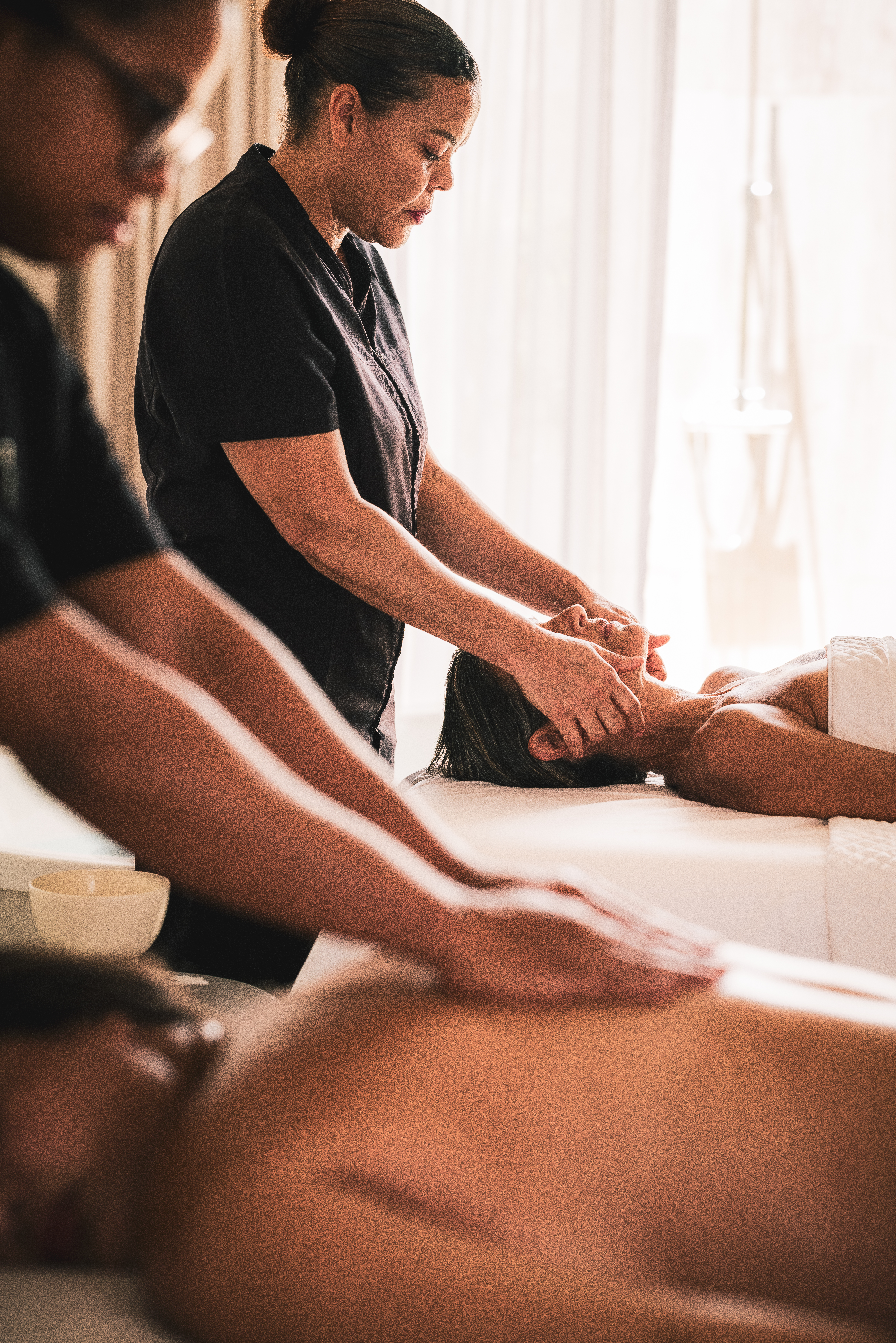 Two therapists providing facial and back massages in a spa setting.