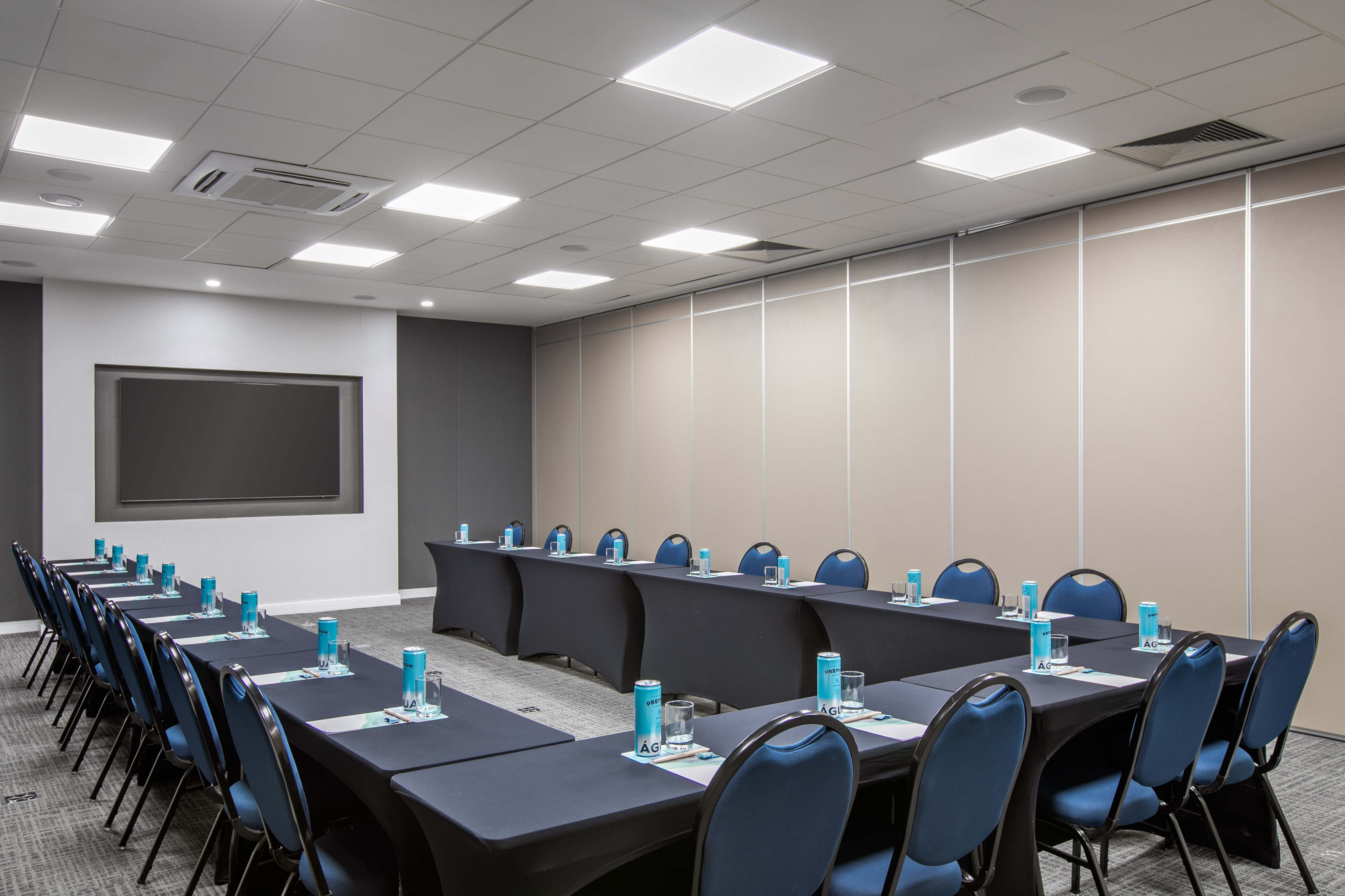 U-shaped conference room with blue chairs, black tables, and a large screen.