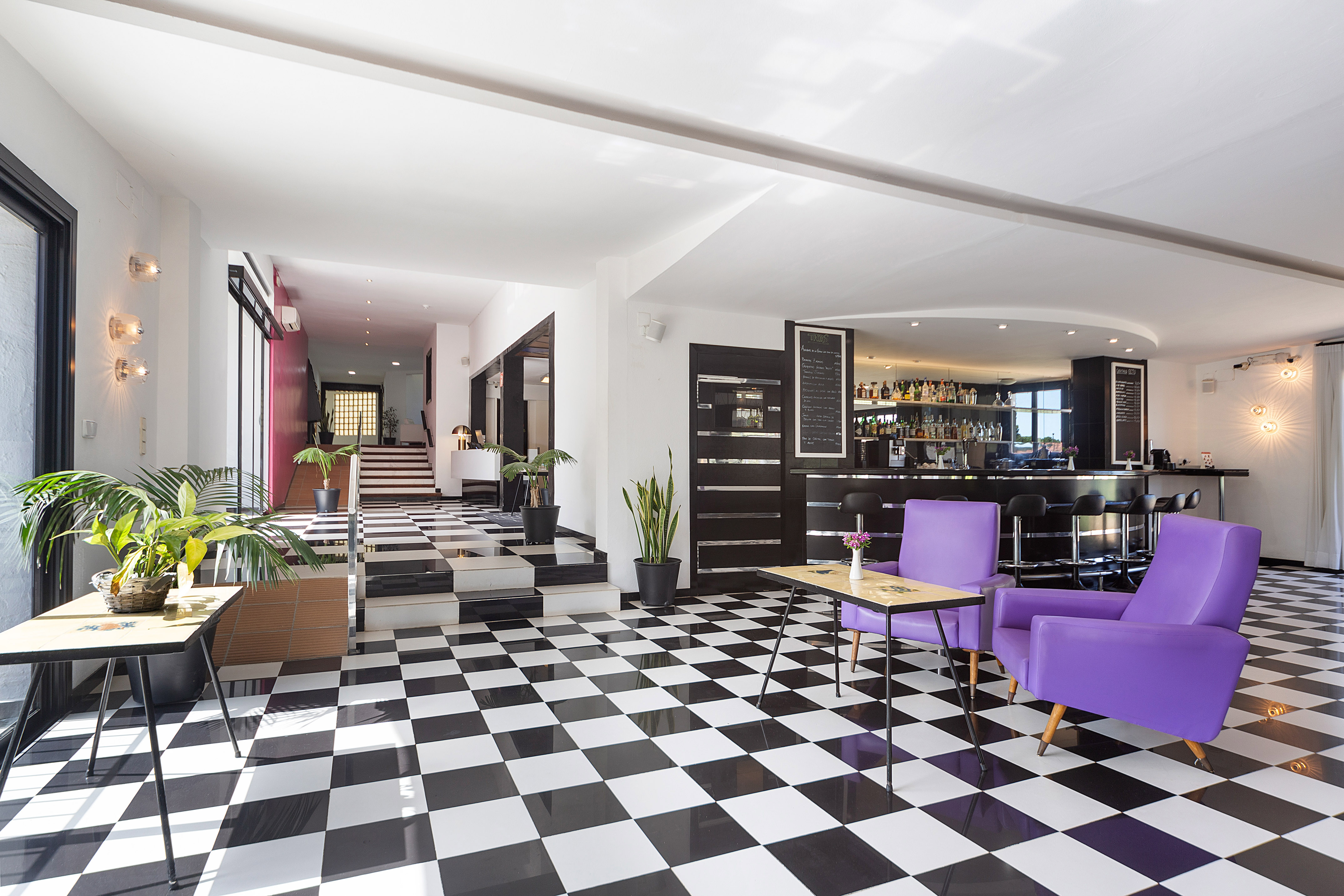 Hotel lobby bar with checkerboard floor, purple armchairs, and modern interior.