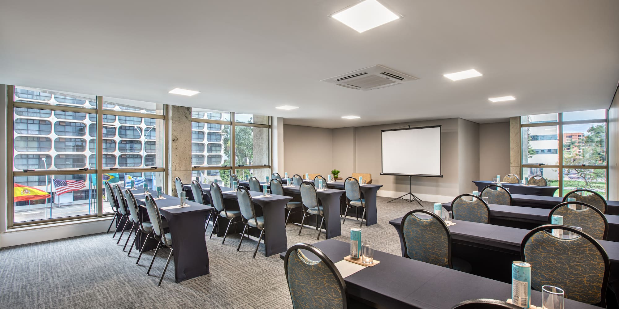 Hotel meeting room with classroom setup, projector screen, and city views.