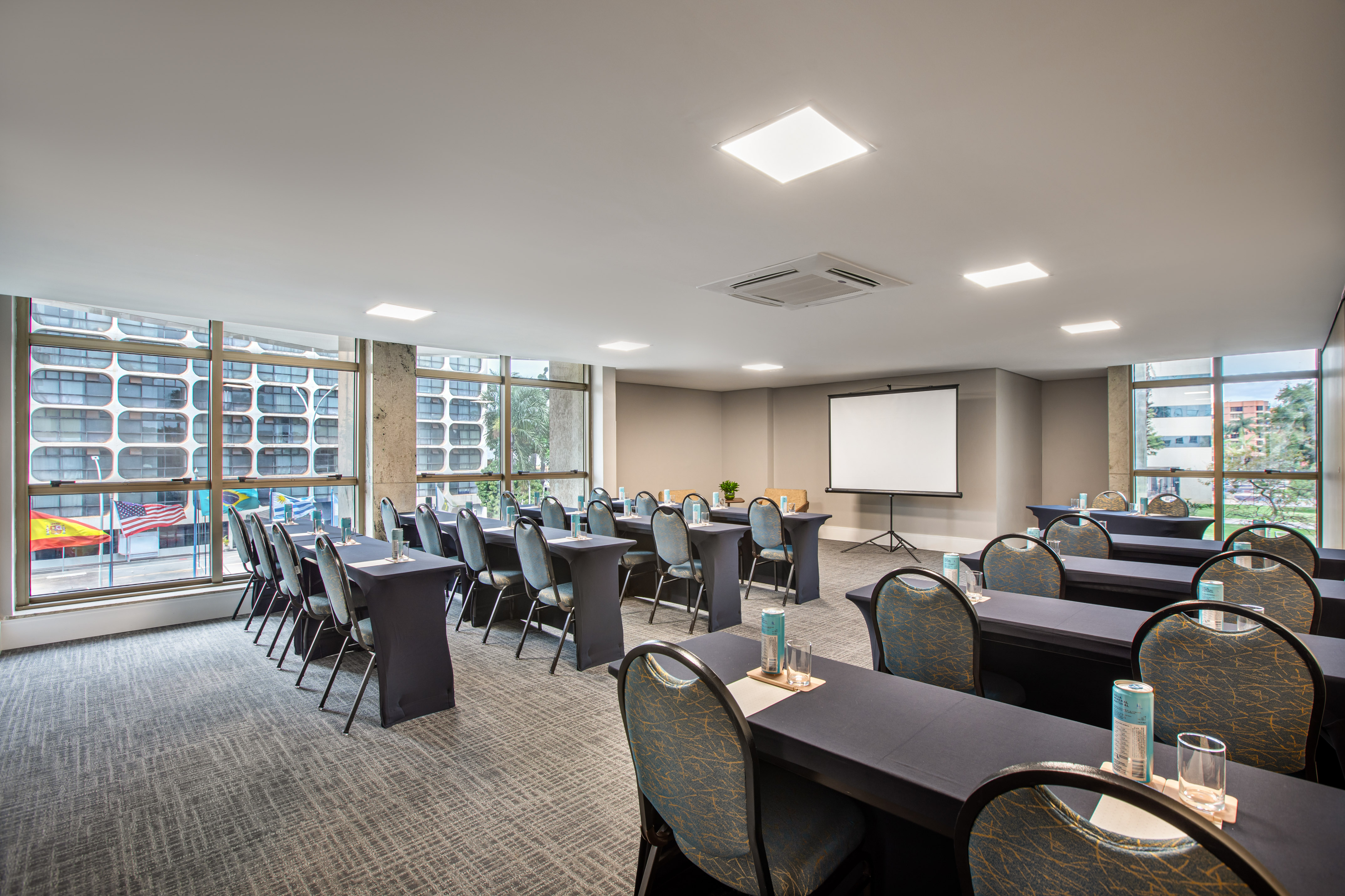 Hotel meeting room with classroom setup, projector screen, and city views.
