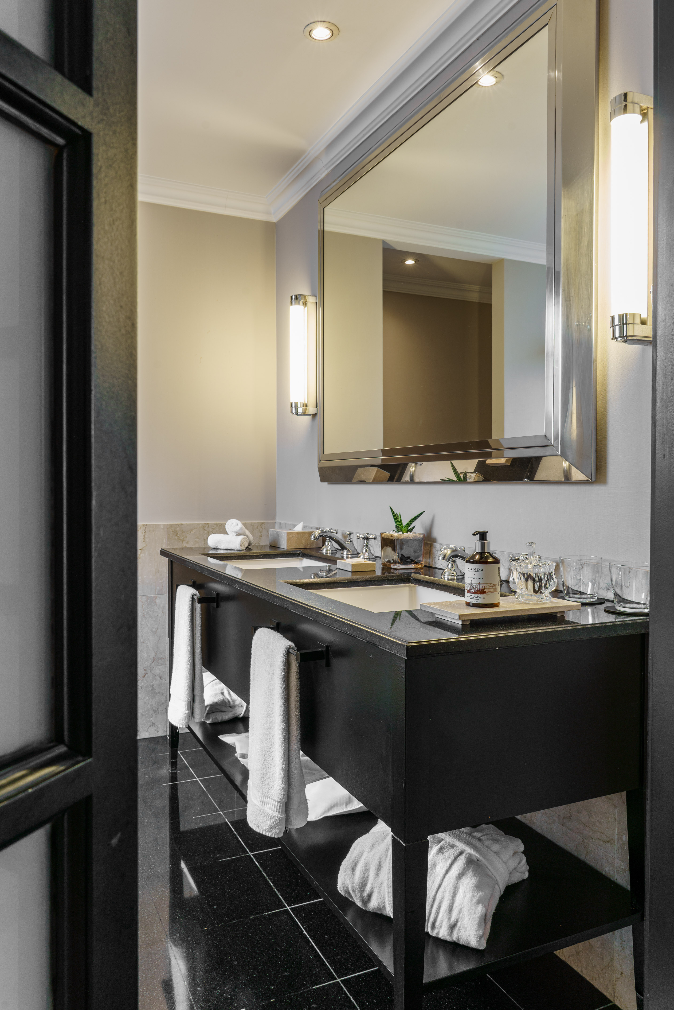Luxury hotel bathroom with black double vanity, large mirror, and white towels.