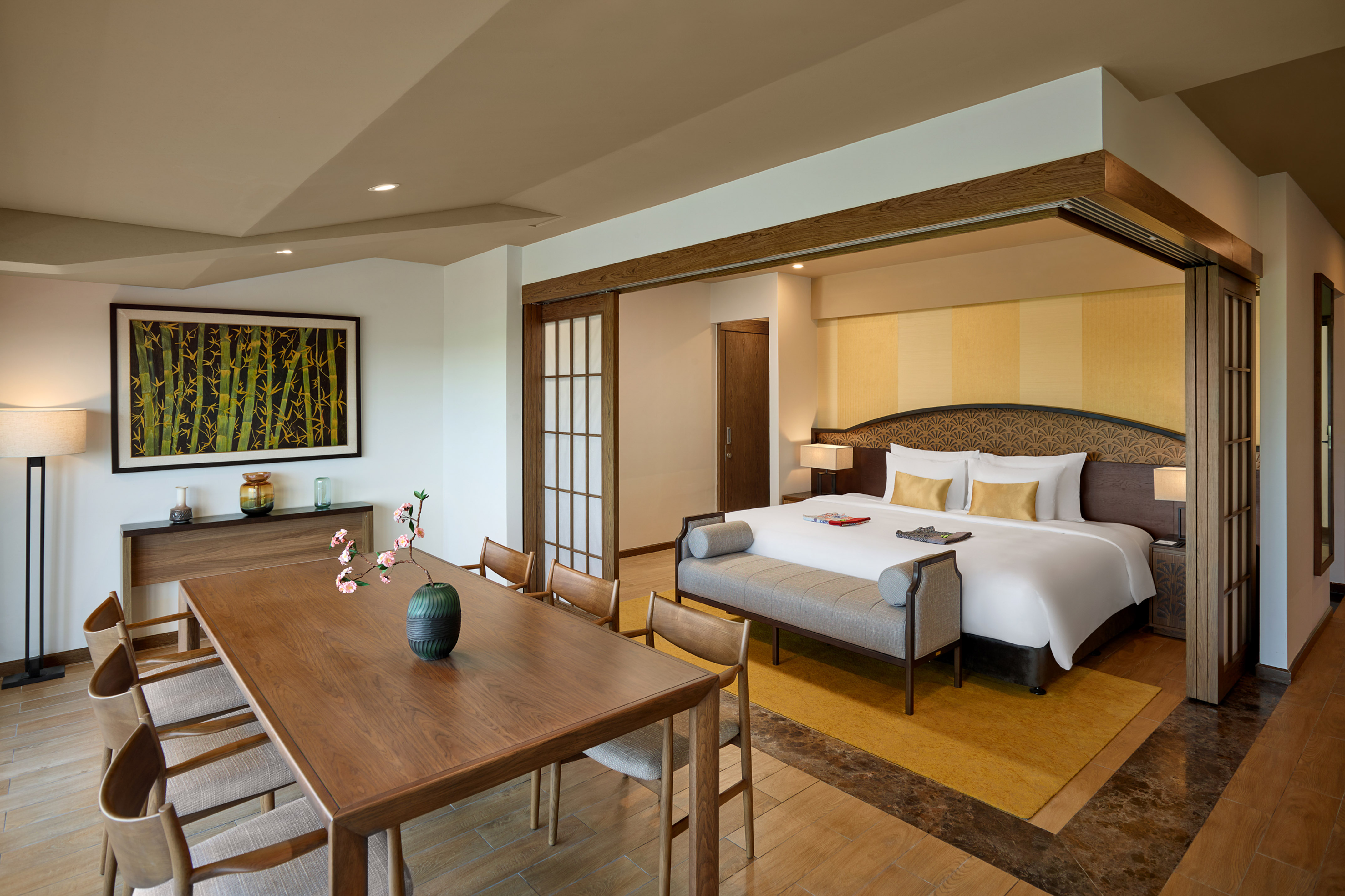 Luxury hotel suite with bedroom, dining area, and bamboo wall art.