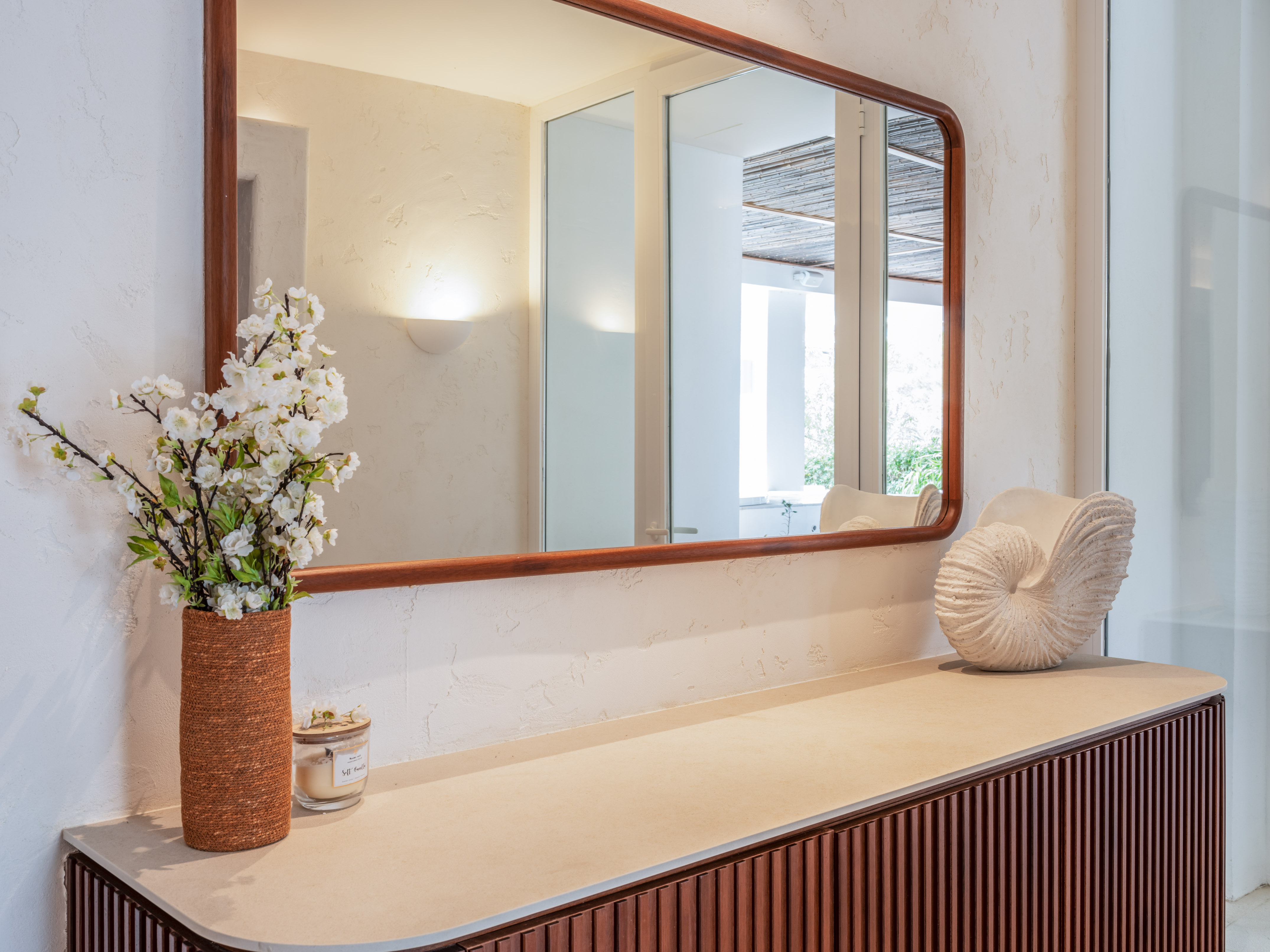 Fluted console table with wooden mirror, white flowers, and shell decor.