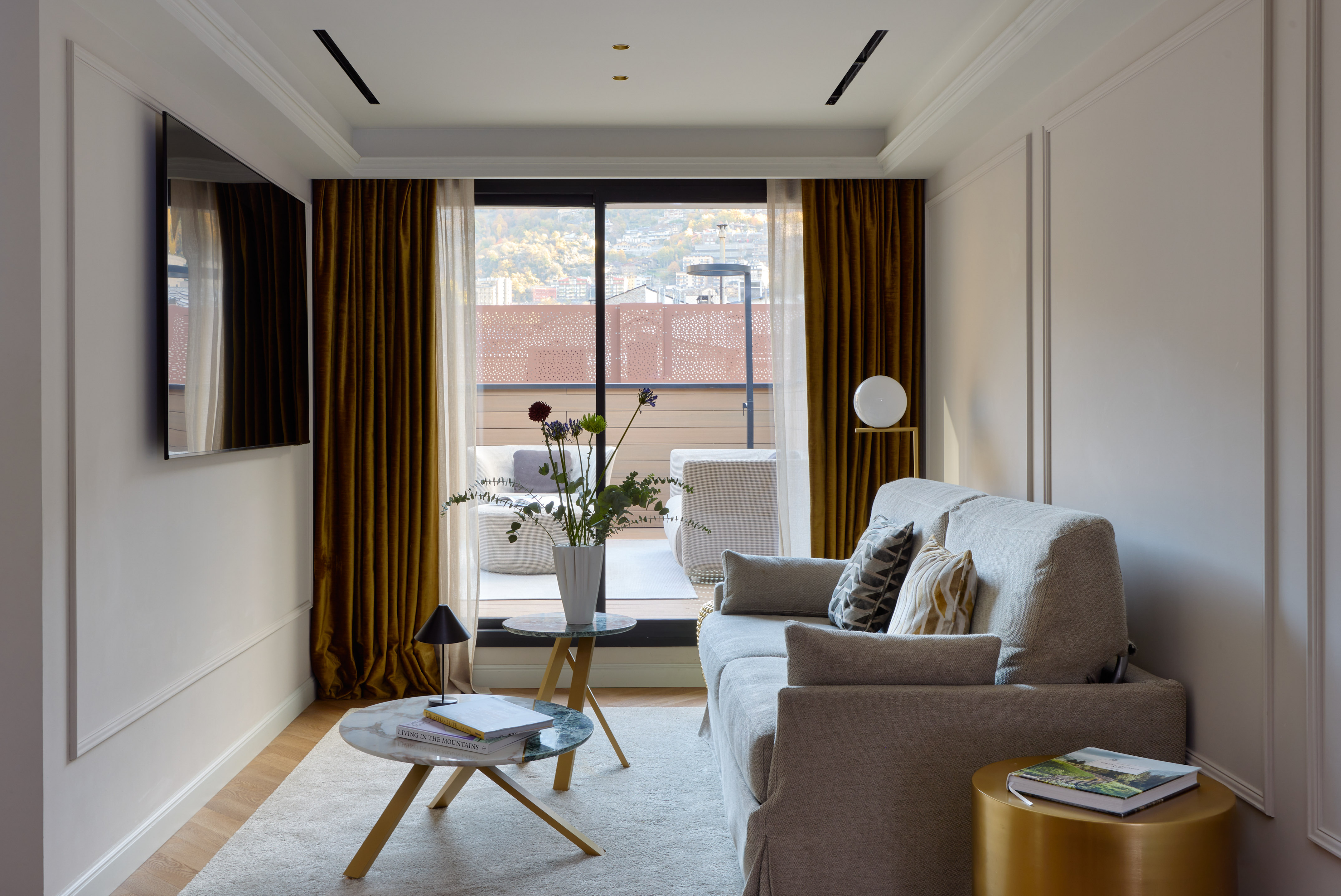 Contemporary living room with sofa, TV, and balcony view of a mountain city.