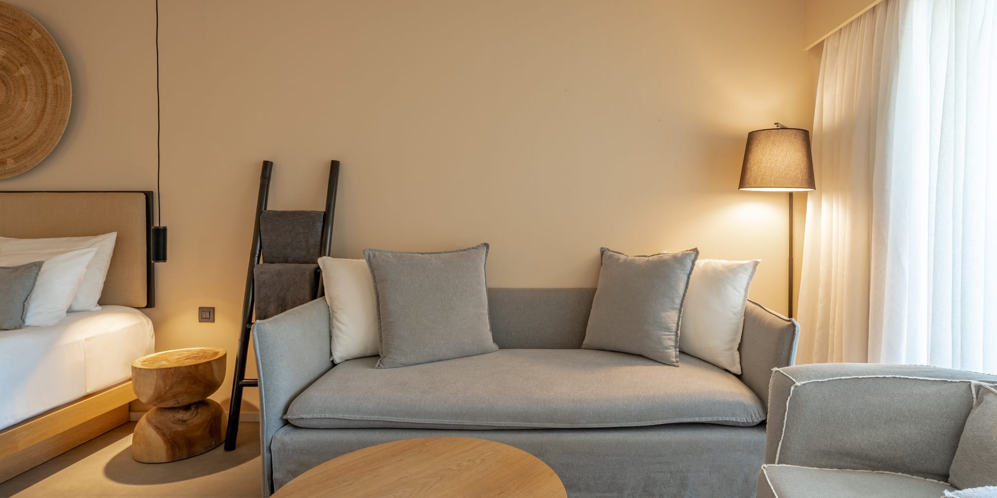 Modern neutral hotel suite with sofa, wooden table, and soft lighting.