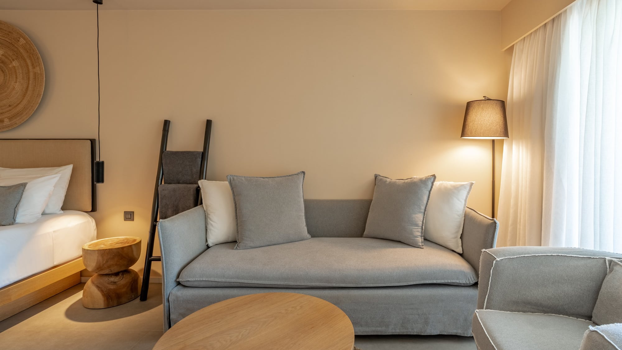 Modern neutral hotel suite with sofa, wooden table, and soft lighting.