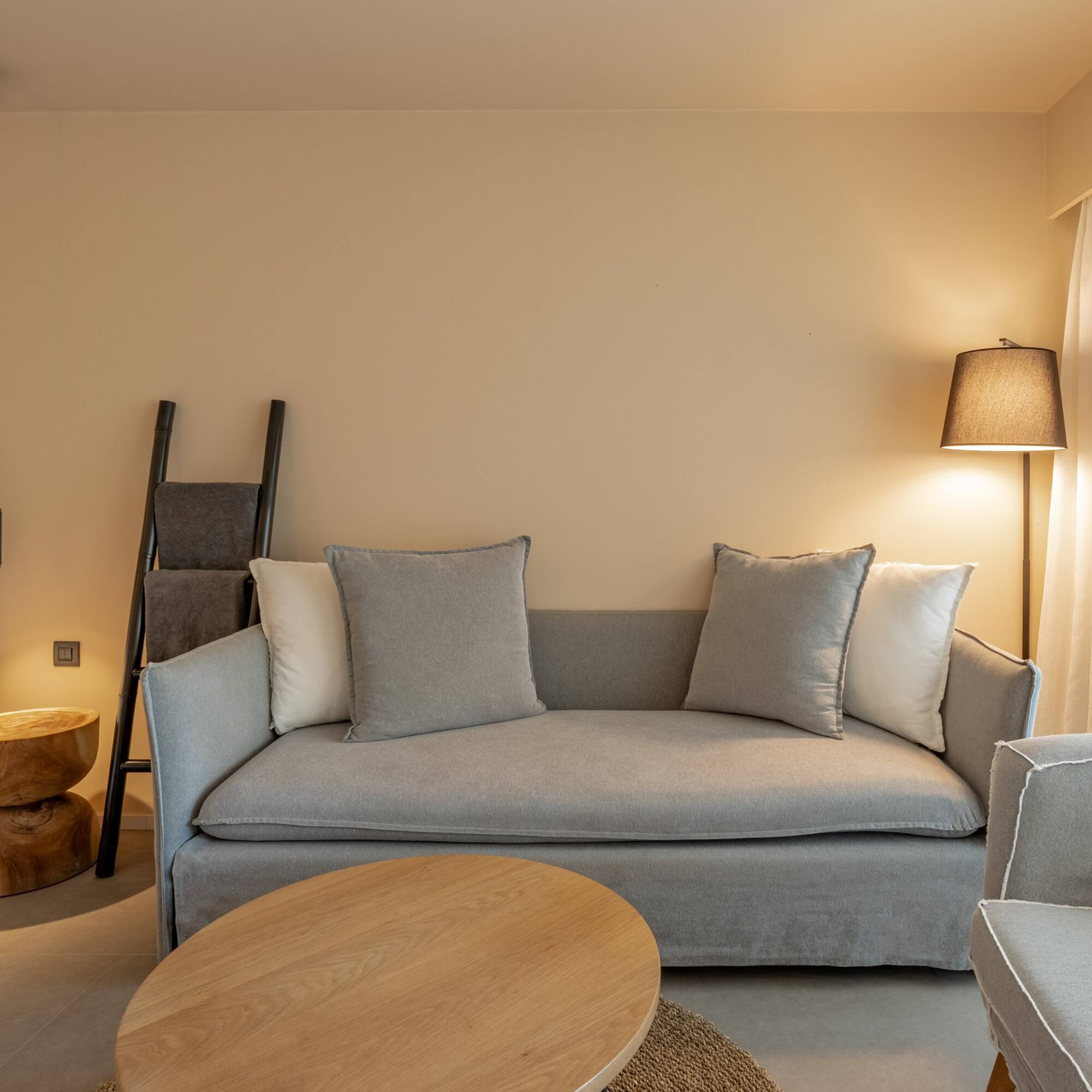 Modern neutral hotel suite with sofa, wooden table, and soft lighting.
