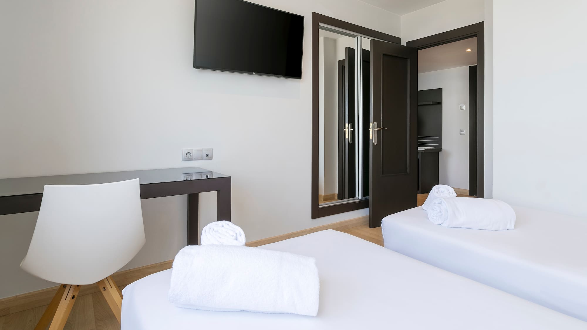 Modern hotel room with twin beds, wall TV, white towels, and desk.