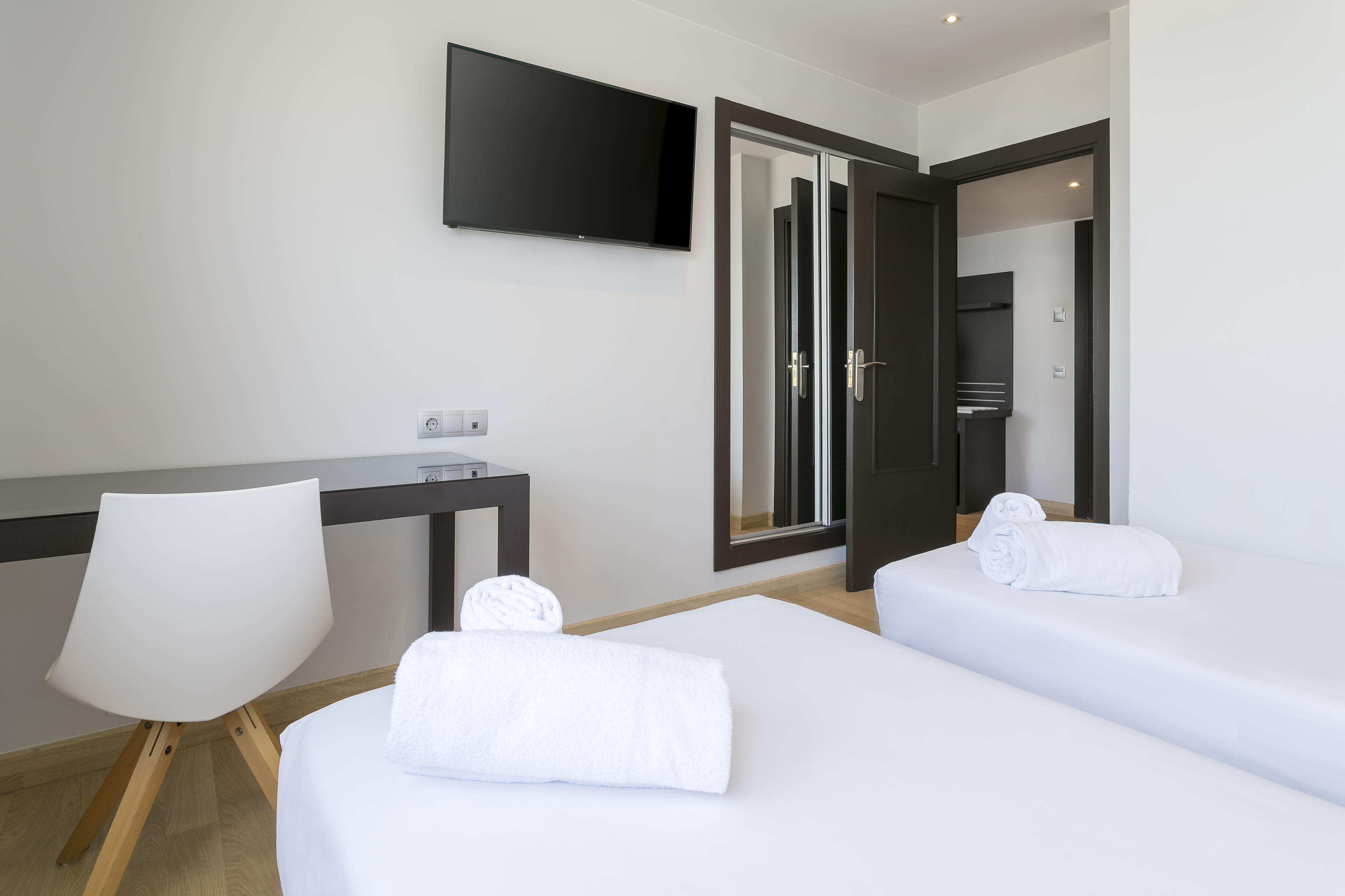 Modern hotel room with twin beds, wall TV, white towels, and desk.