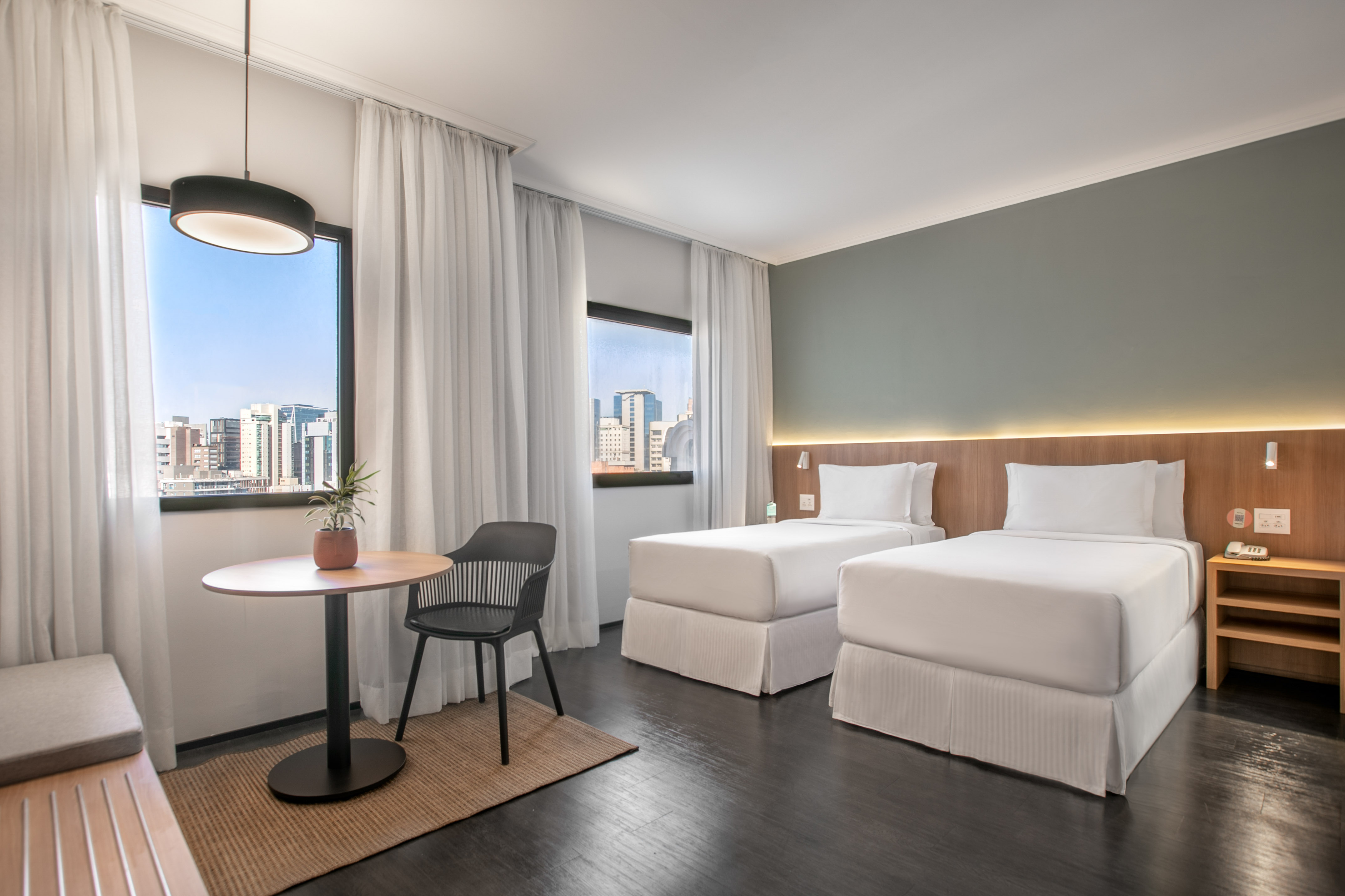 Twin hotel room with city view, modern design, and dark wood floors.