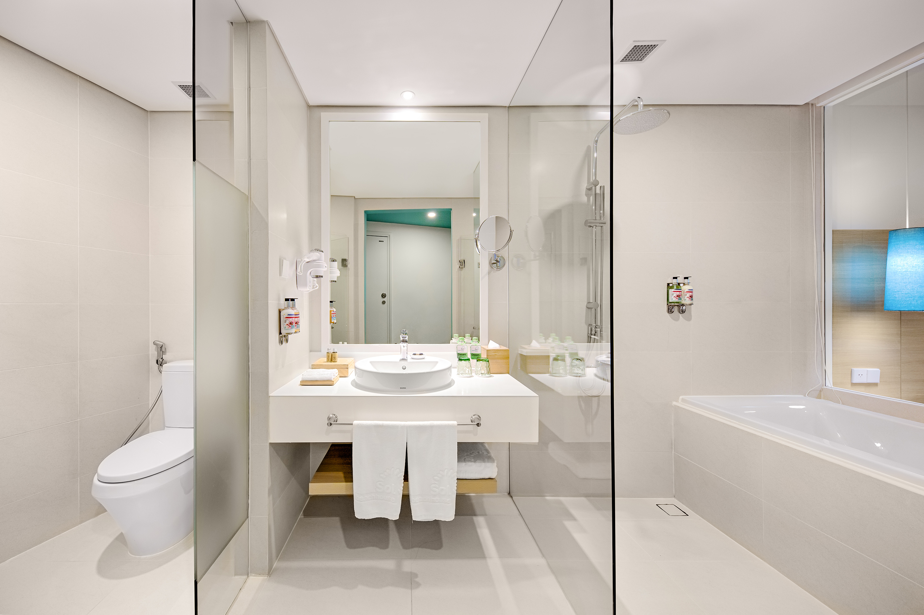 Modern white hotel bathroom with vanity, toilet, shower, and bathtub.