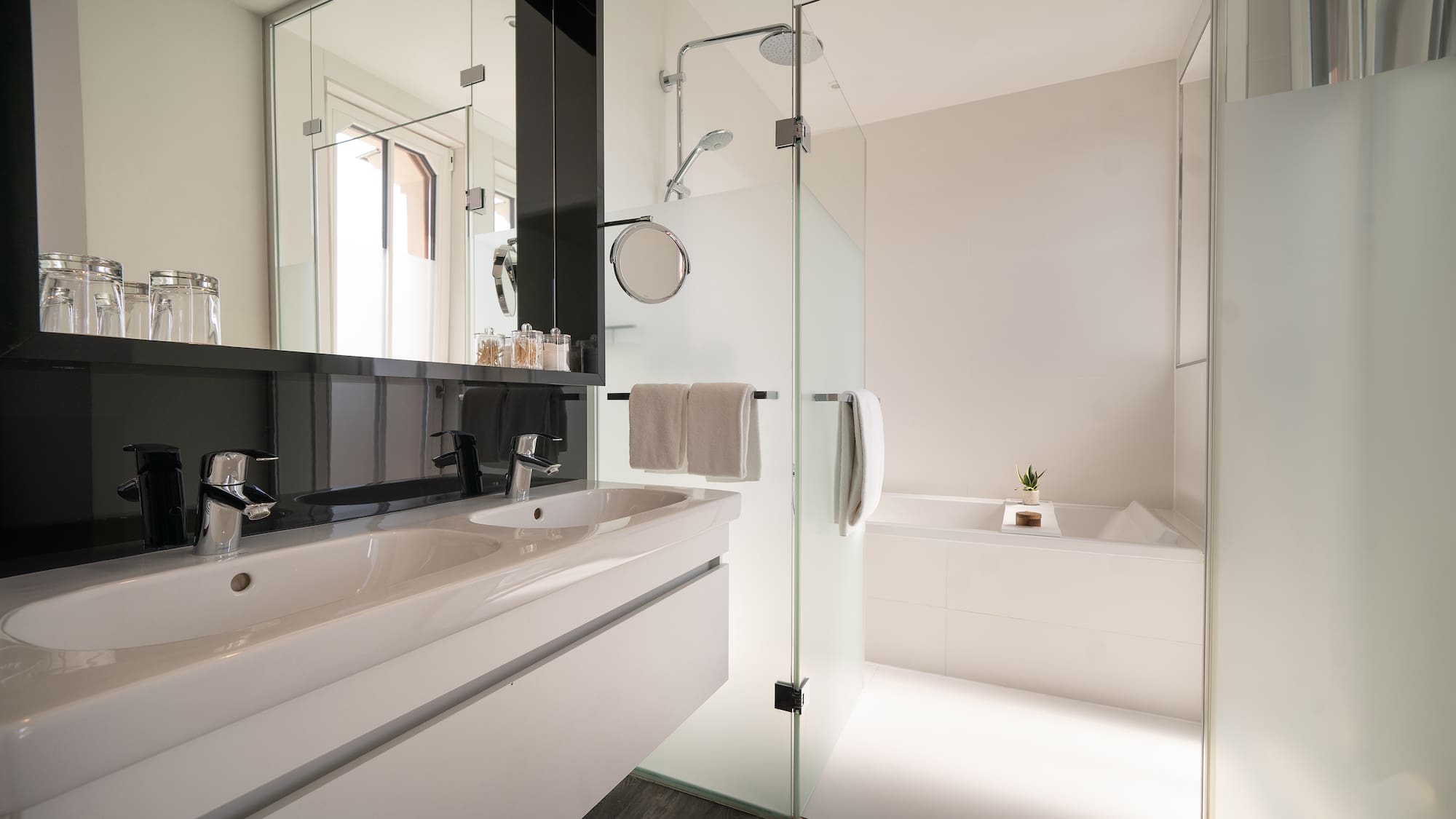 Modern bathroom with double vanity, walk-in glass shower, and bathtub.