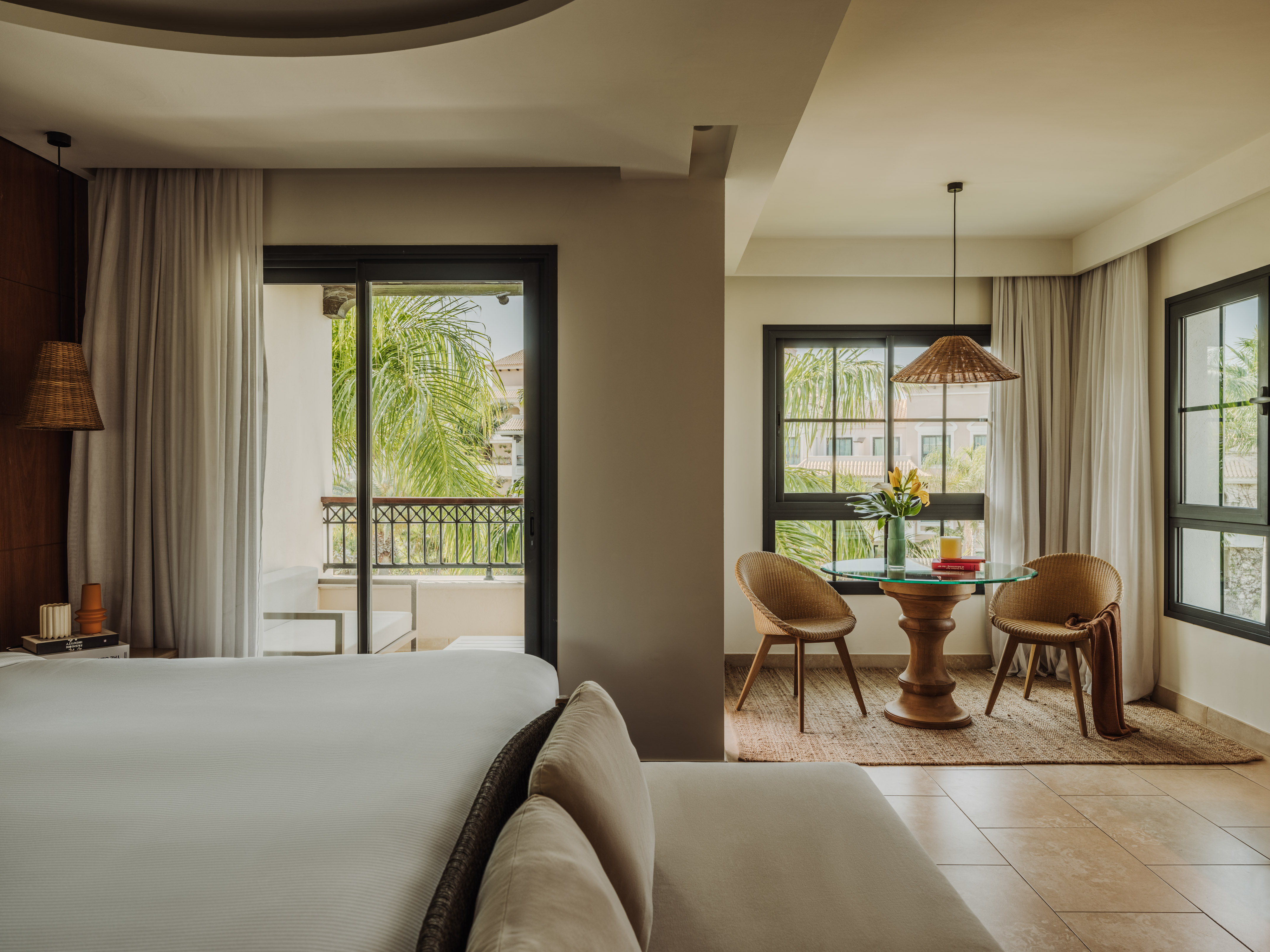 Modern resort room with bed, balcony to tropical palms, and dining area.