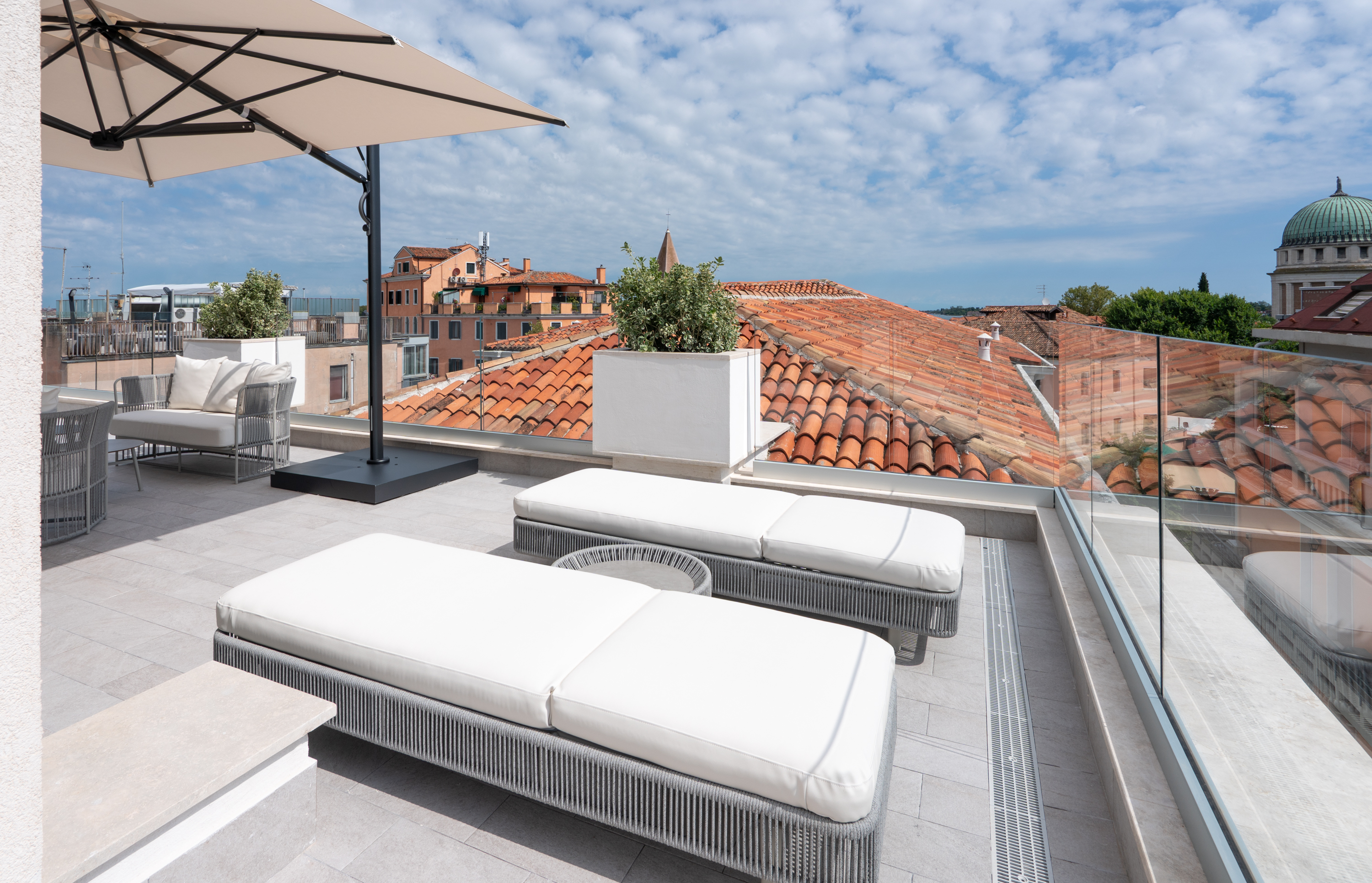 Modern rooftop terrace with loungers, umbrella, and red tile city view.