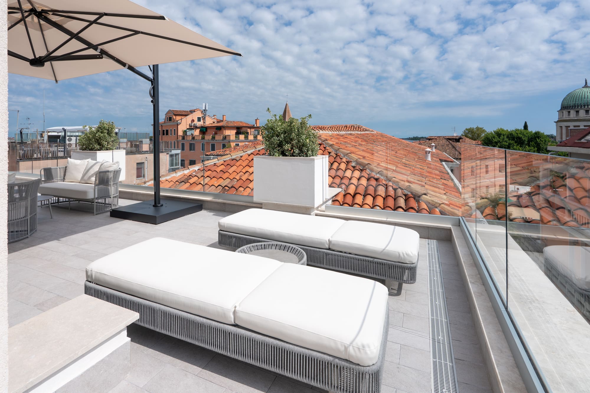 Modern rooftop terrace with loungers, umbrella, and red tile city view.