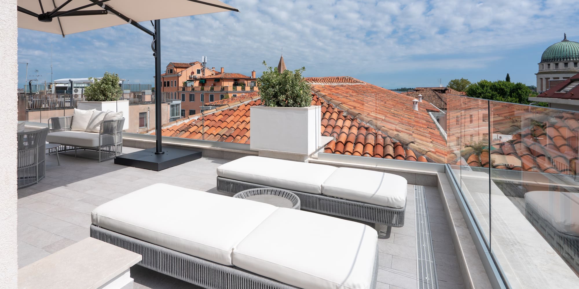 Modern rooftop terrace with loungers, umbrella, and red tile city view.