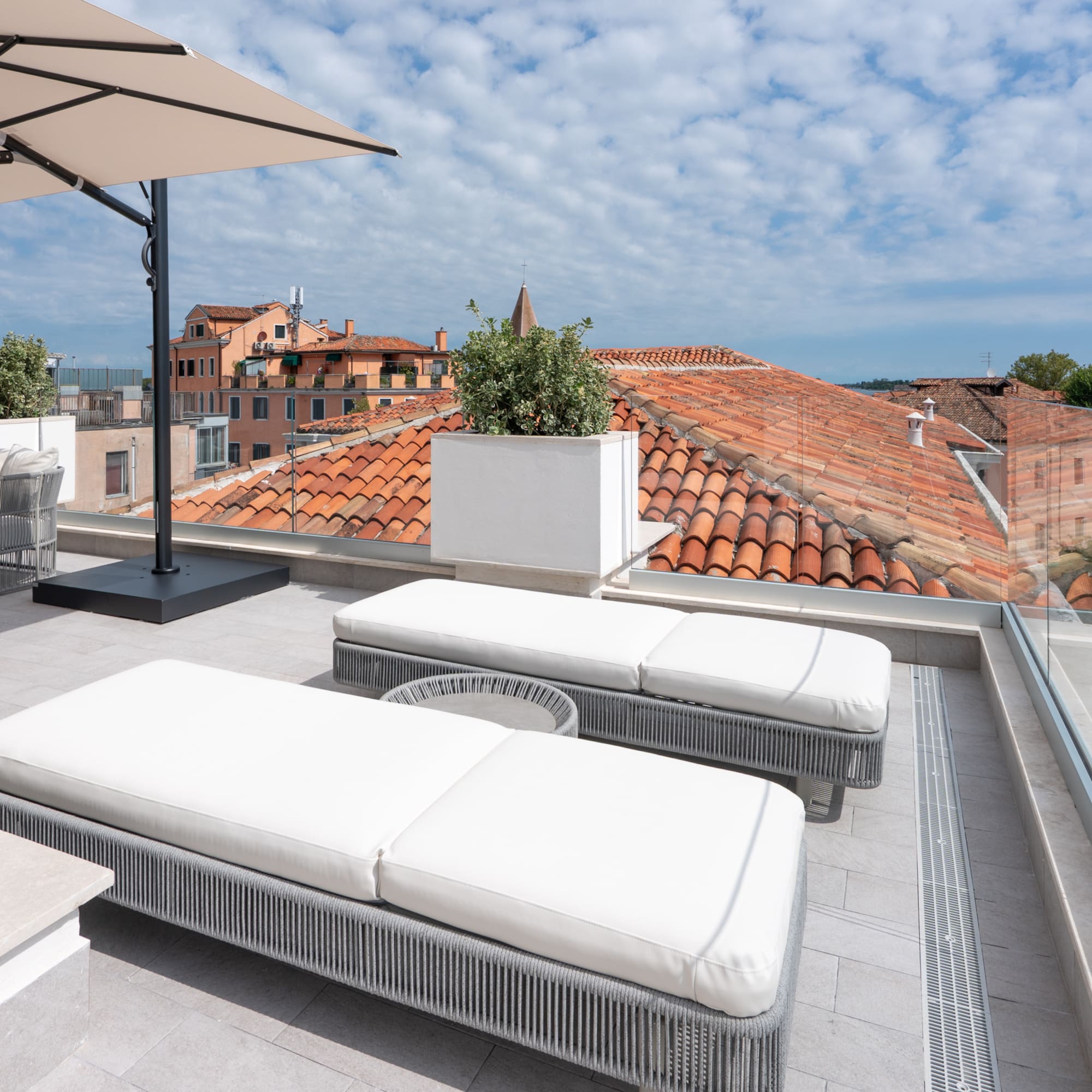 Modern rooftop terrace with loungers, umbrella, and red tile city view.