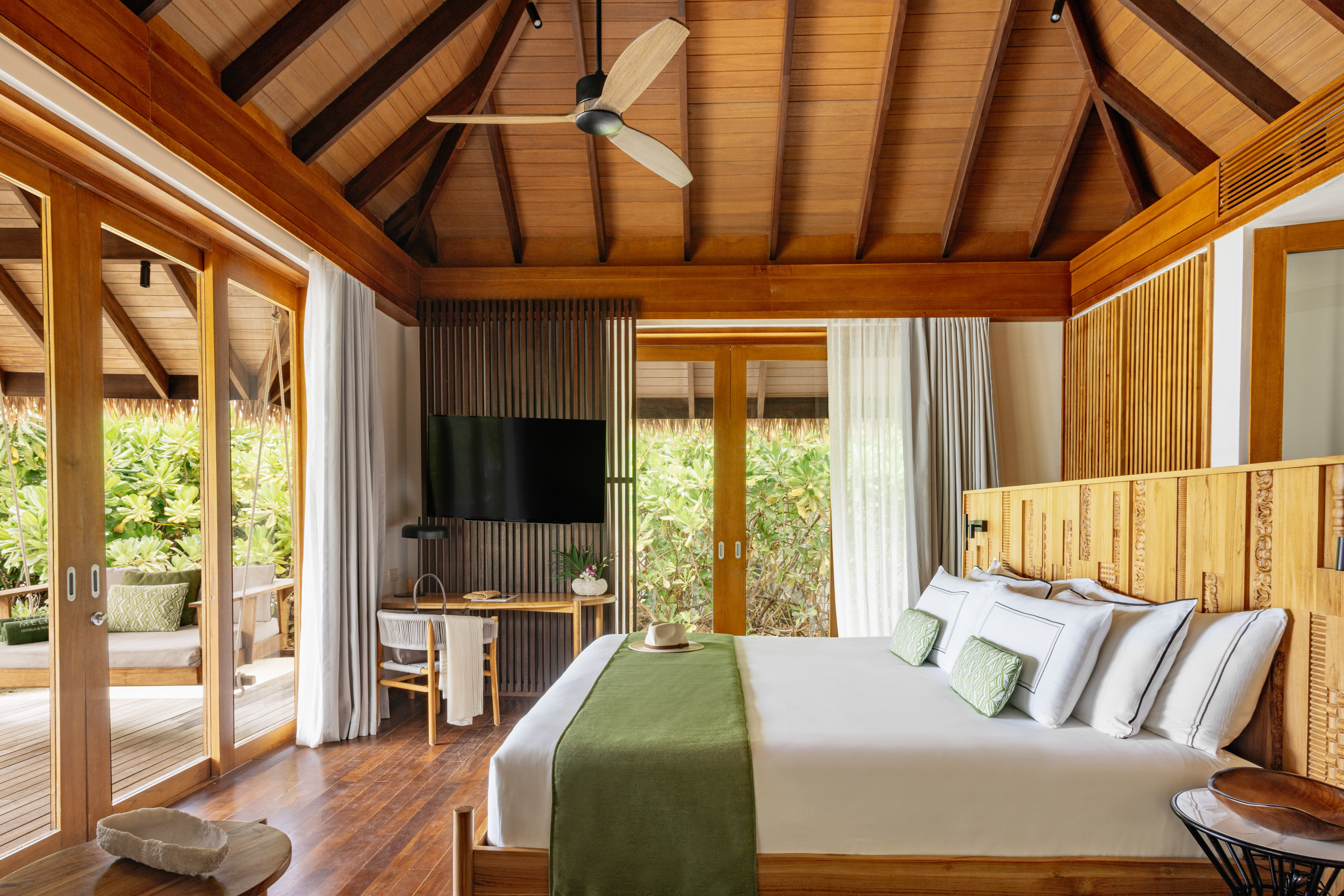 Luxury tropical resort bedroom with king bed, wooden ceiling, and patio view.