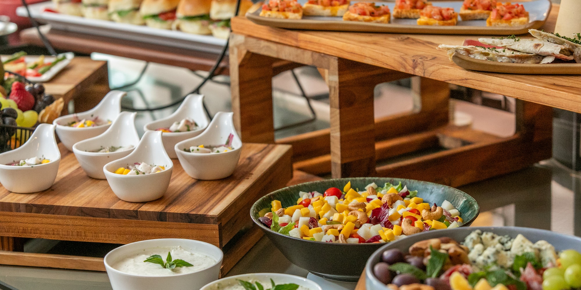 Varied buffet spread with sliders, bruschetta, salads, ceviche, and dips.