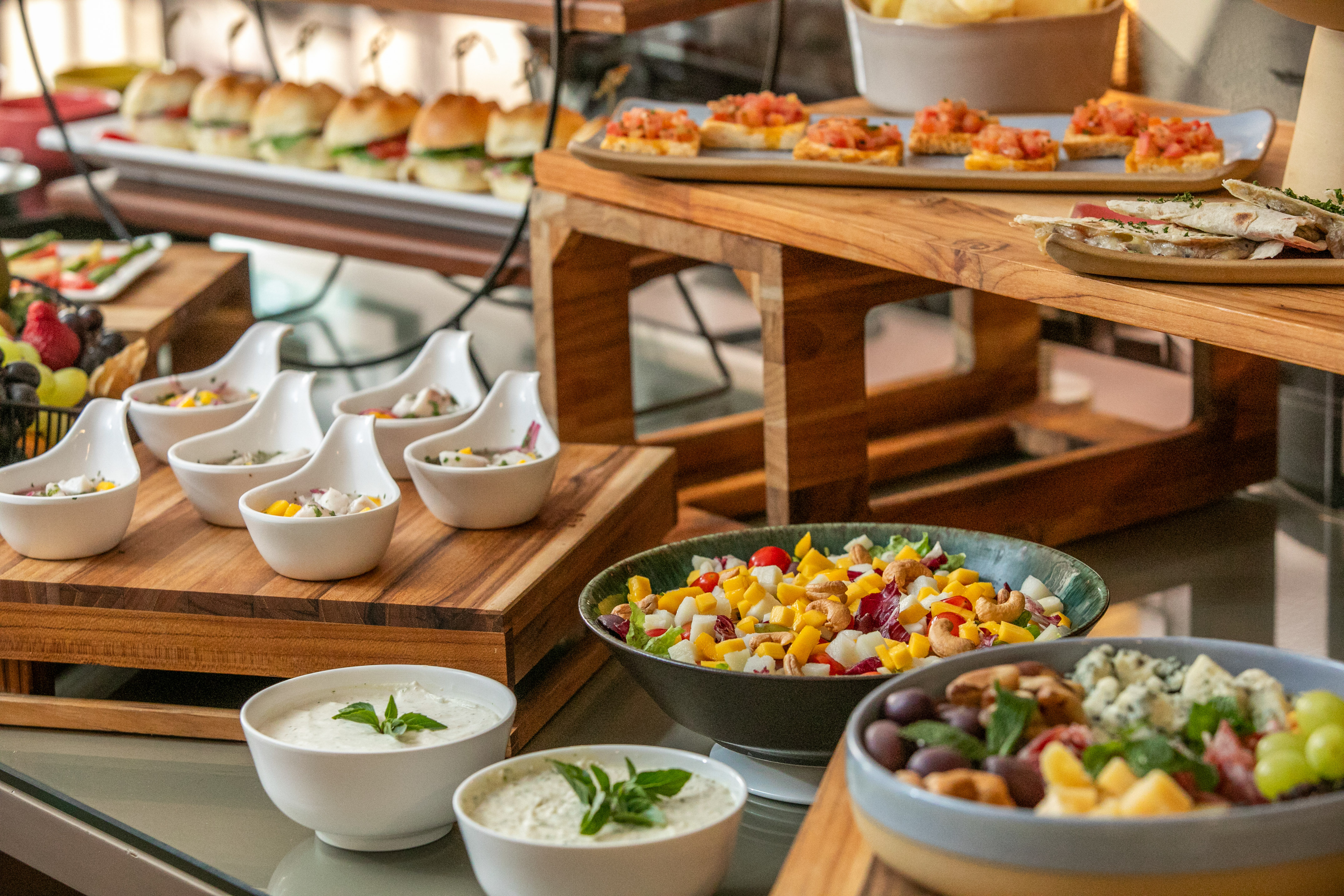 Varied buffet spread with sliders, bruschetta, salads, ceviche, and dips.