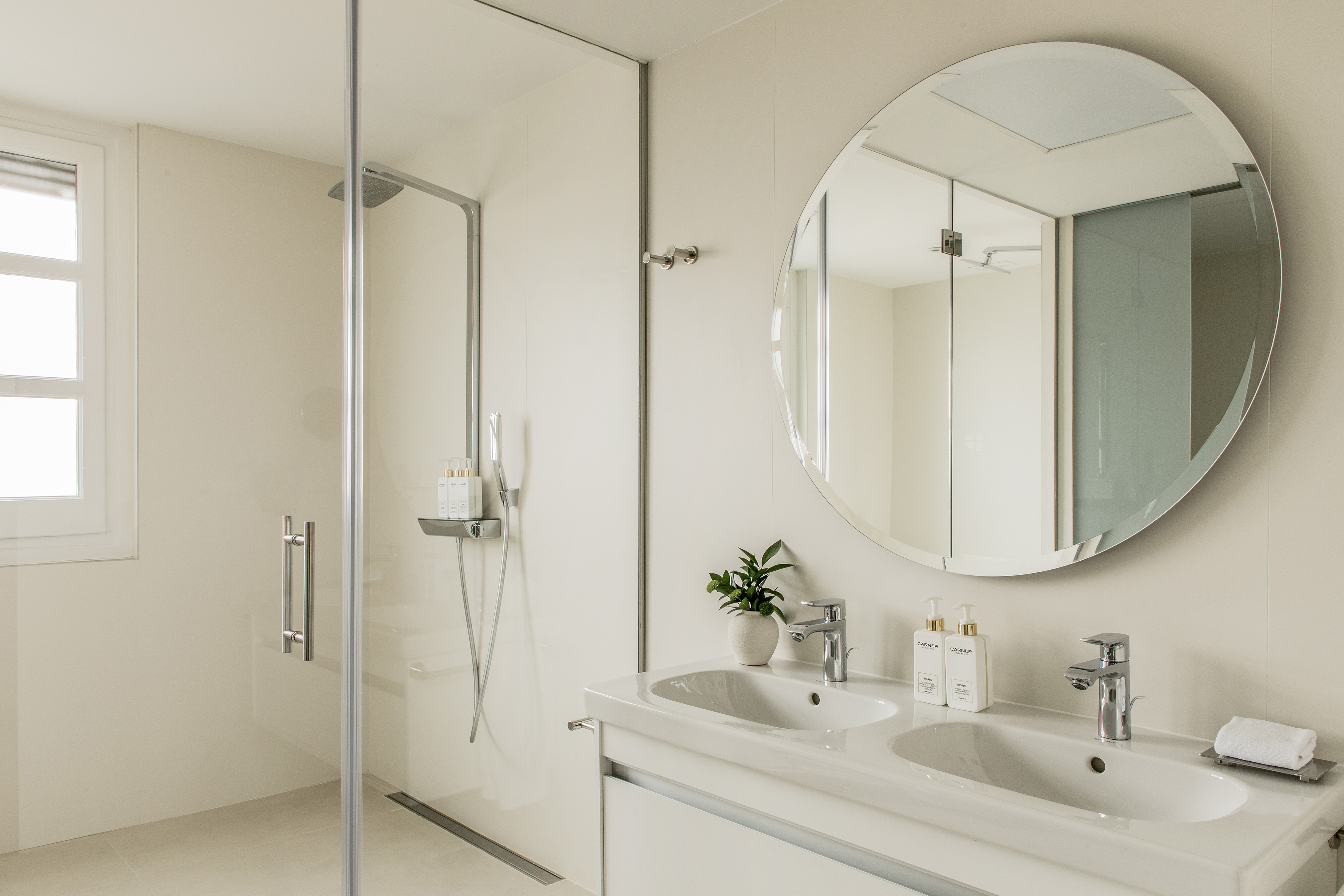 Sleek modern bathroom with double vanity, round mirror, glass walk-in shower.