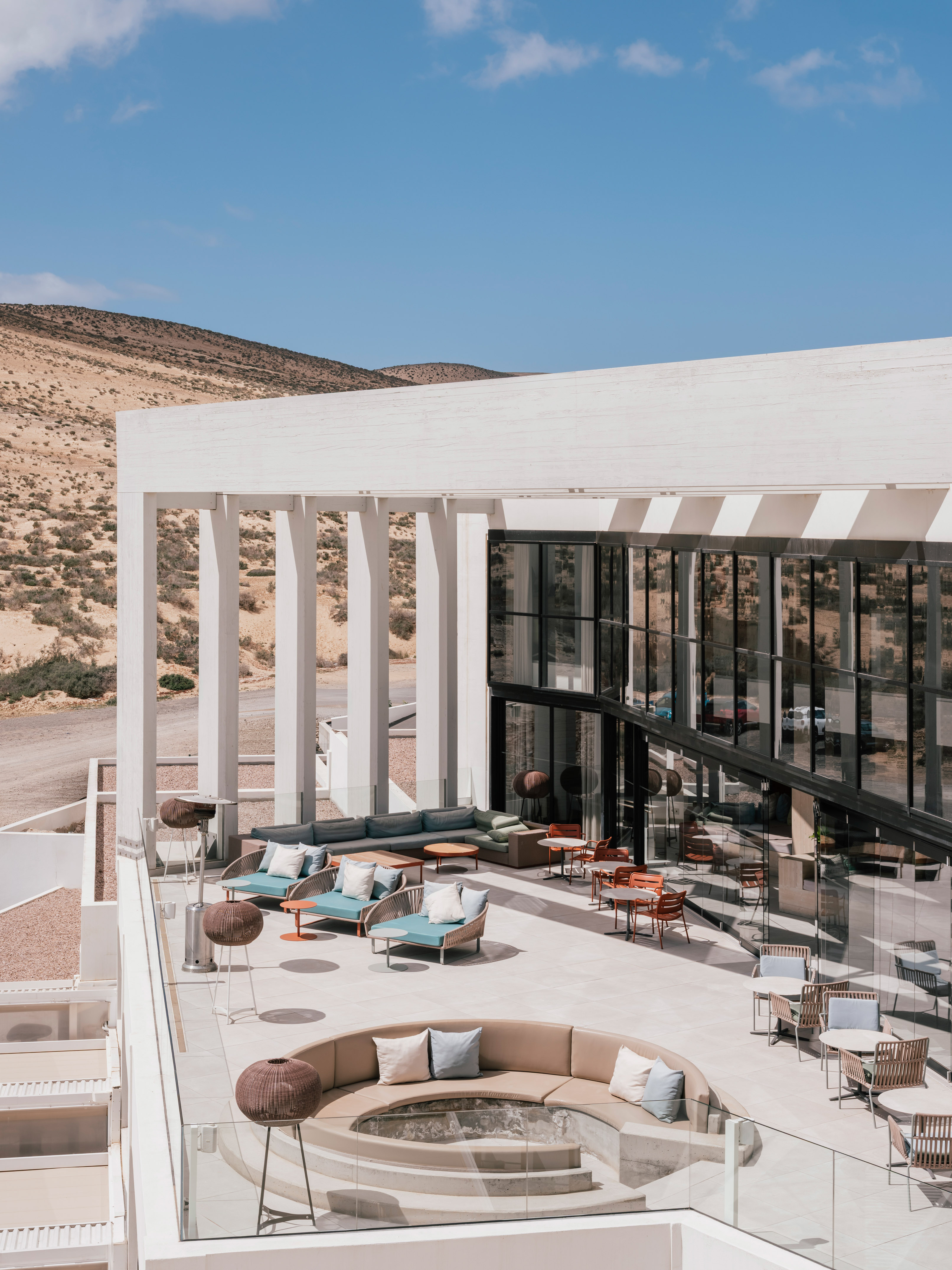 Modern outdoor terrace with lounge seating, fire pit, and desert backdrop.