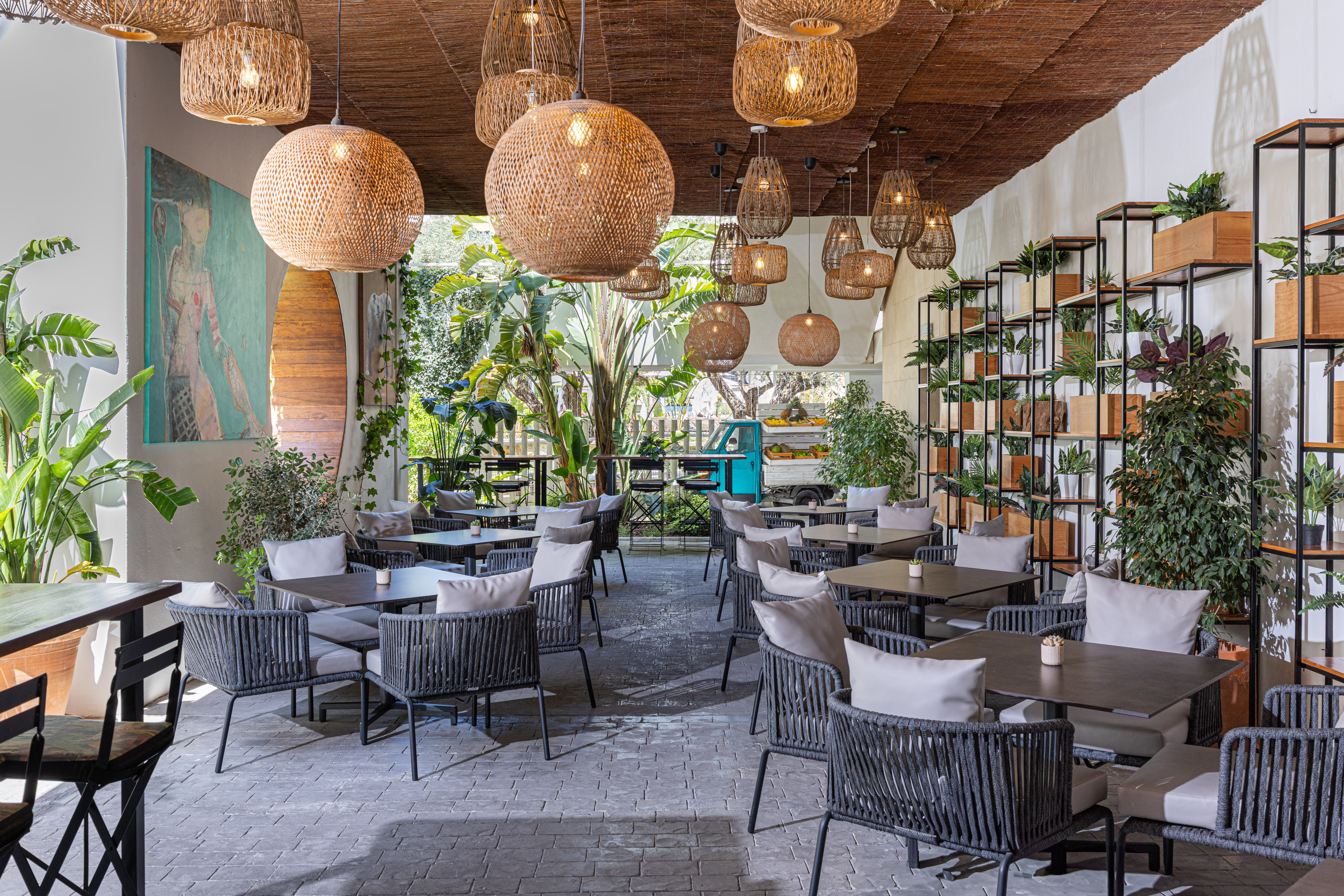 Outdoor restaurant patio with woven lights, tropical plants, and modern seating.