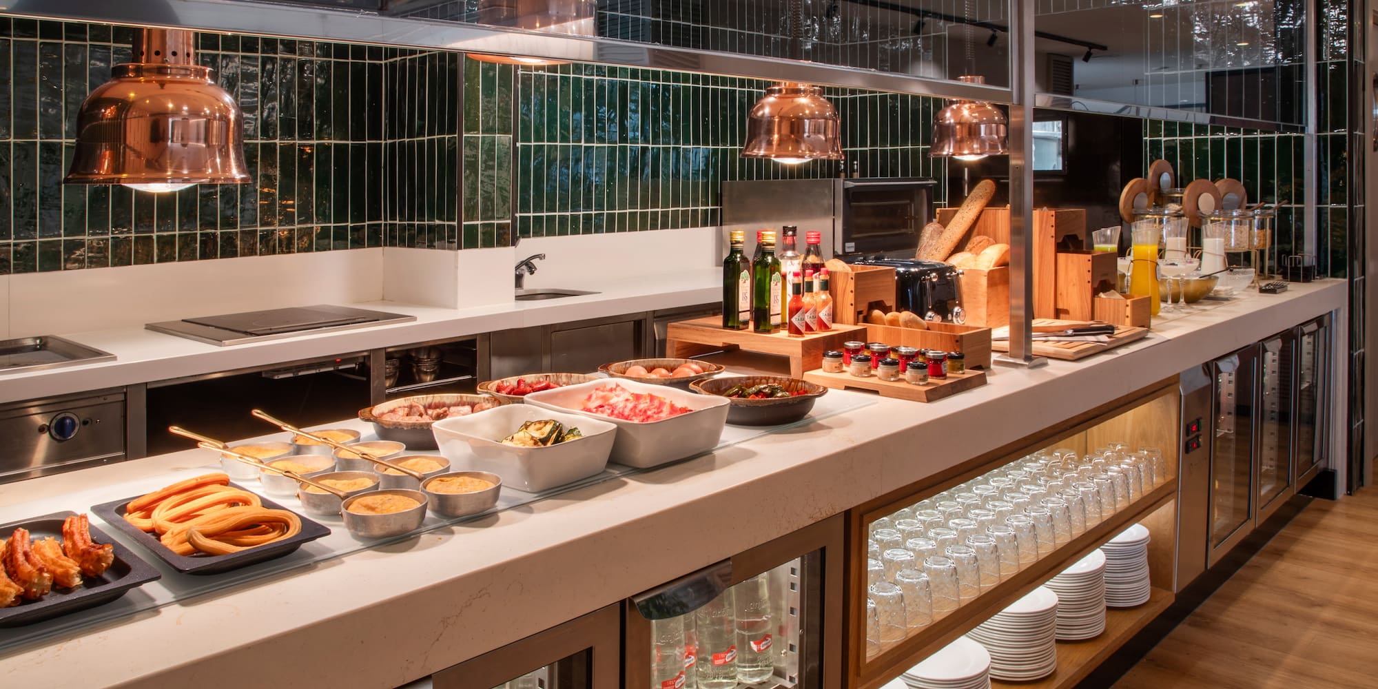 Breakfast buffet counter with churros, bacon, eggs, bread, jams, and juices.